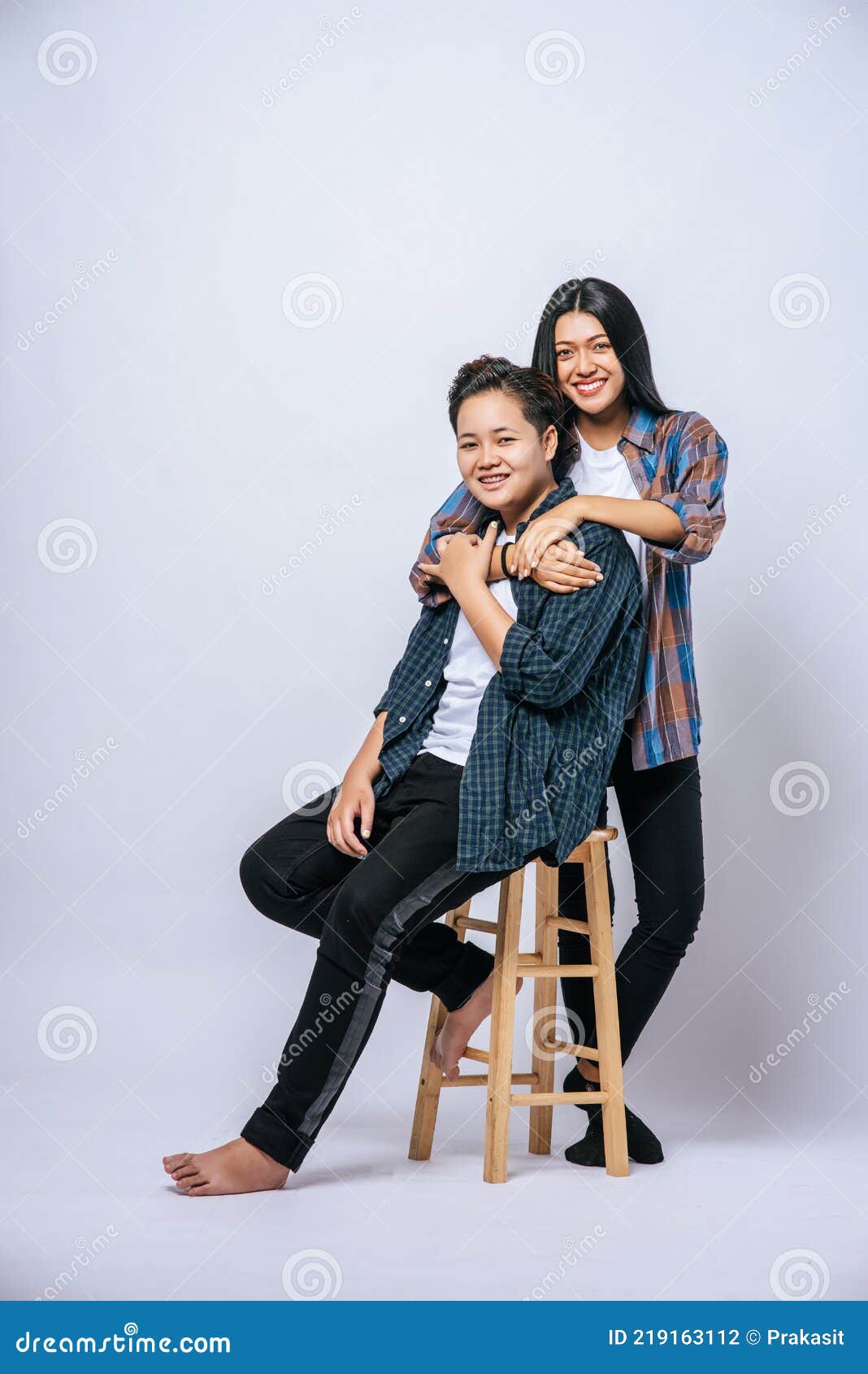 Two Women Lovers Grab Another Shoulder and Sit in a Chair Stock Photo
