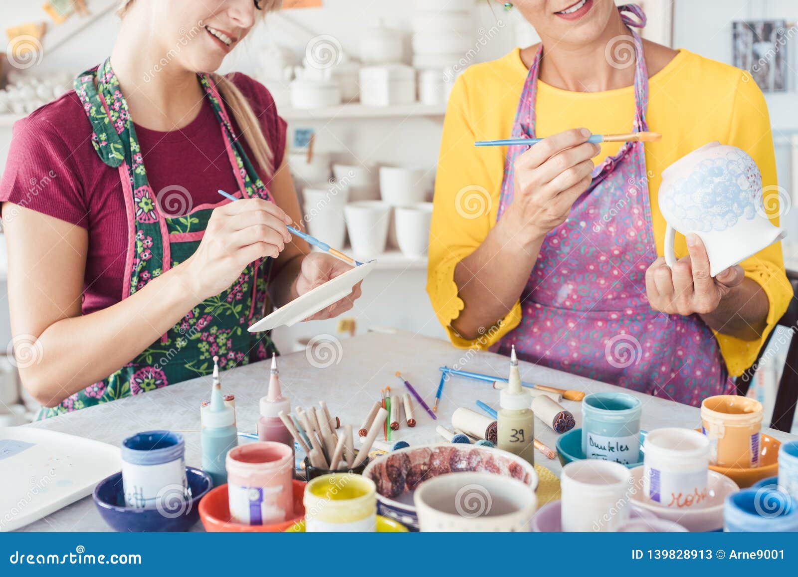 two women painting own ceramic tableware in diy workshop