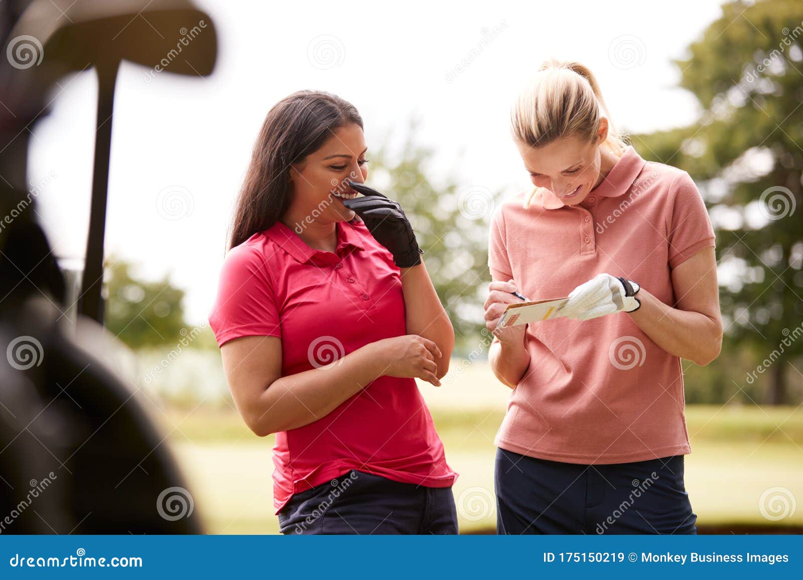 Two Women Playing Golf Marking Scorecard with Buggy in Foreground Stock
