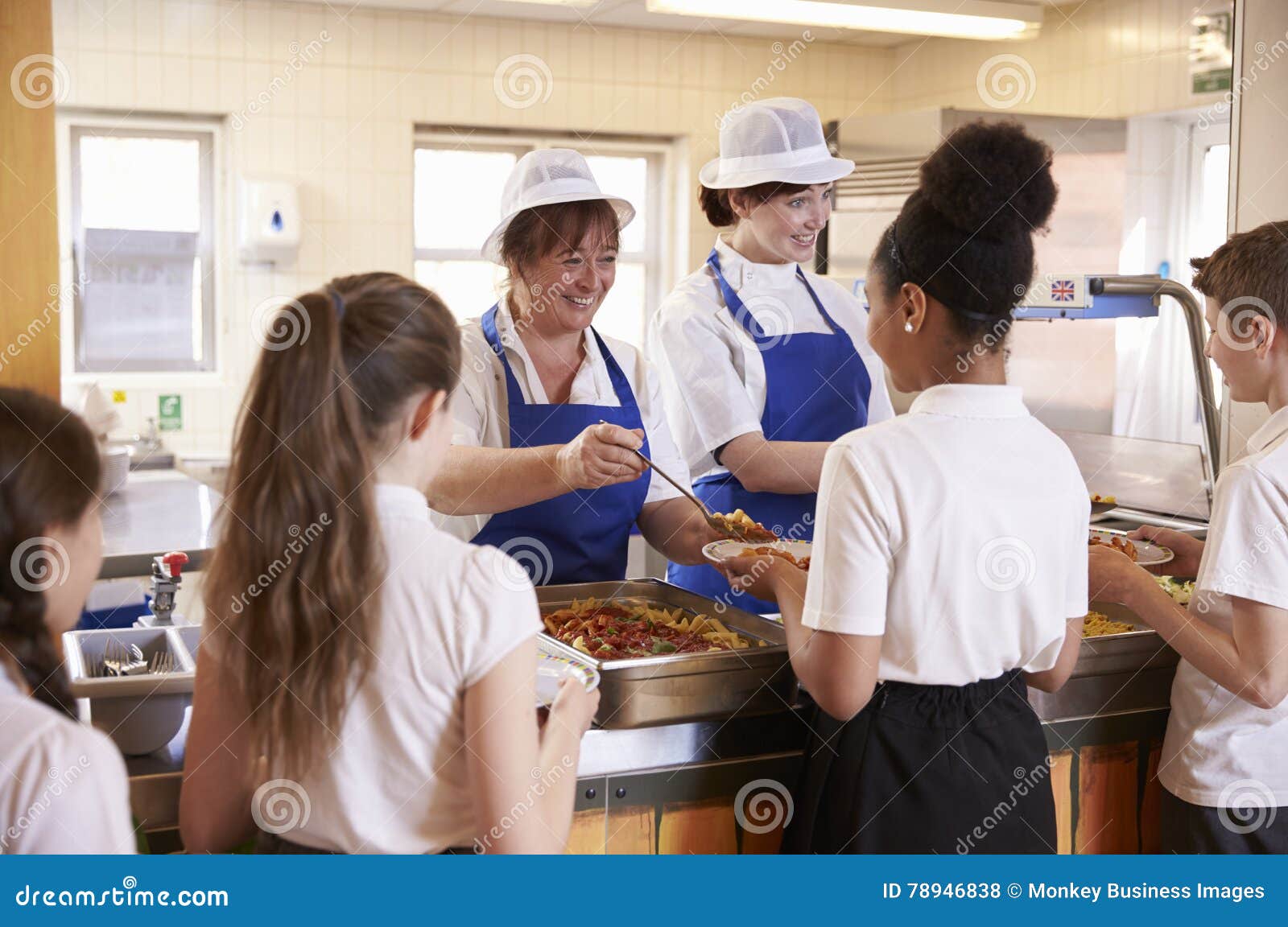 two women serving kids food in a school cafeteria, back view