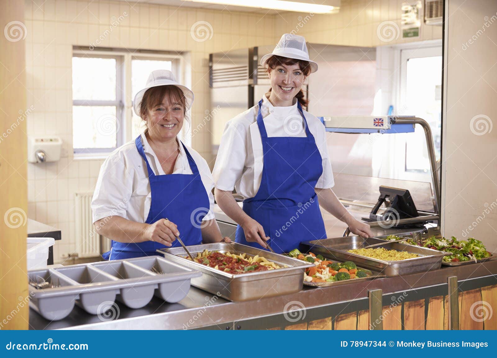 two women waiting to serve lunch in a school cafeteria