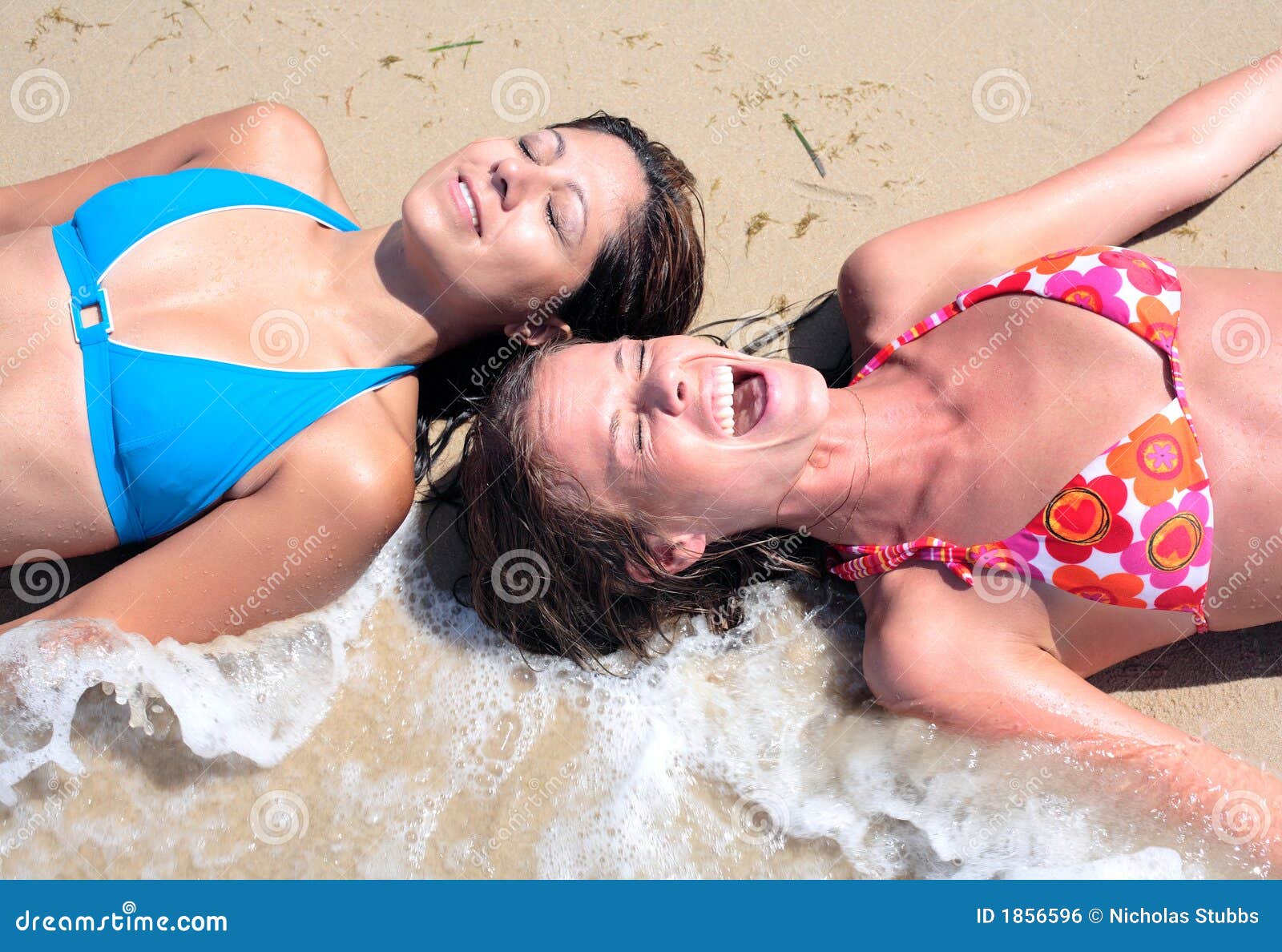 two young attractive women splashed by cold wave on the beach