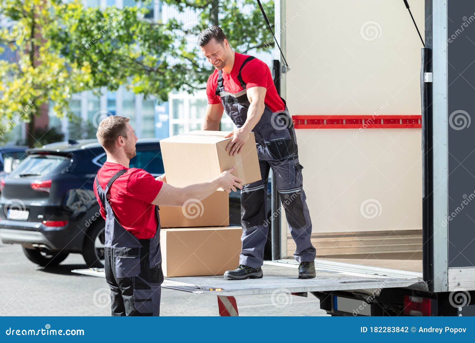 two young male movers carrying cardboard boxes from truck