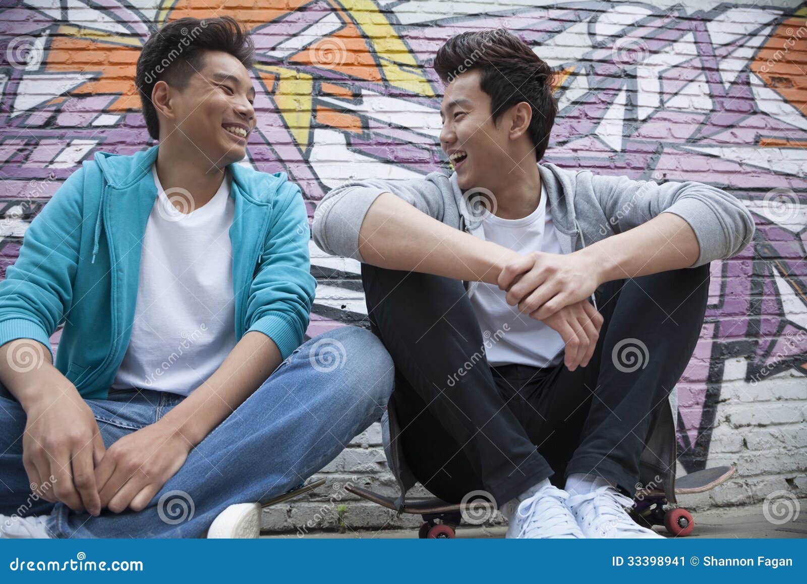 Two Young Men Sitting on Their Skateboards and Hanging Out in Front of
