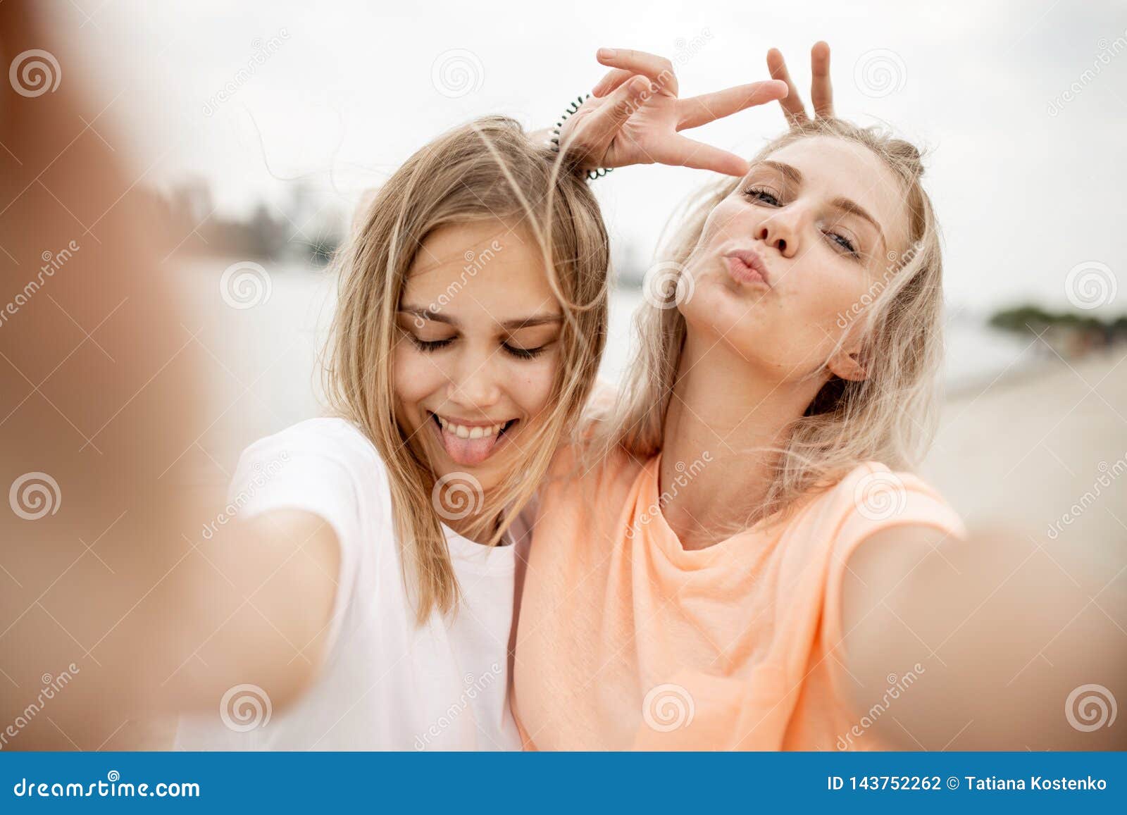 Two Young Pretty Blonde Girls Take A Selfie On The Beach On A Warm