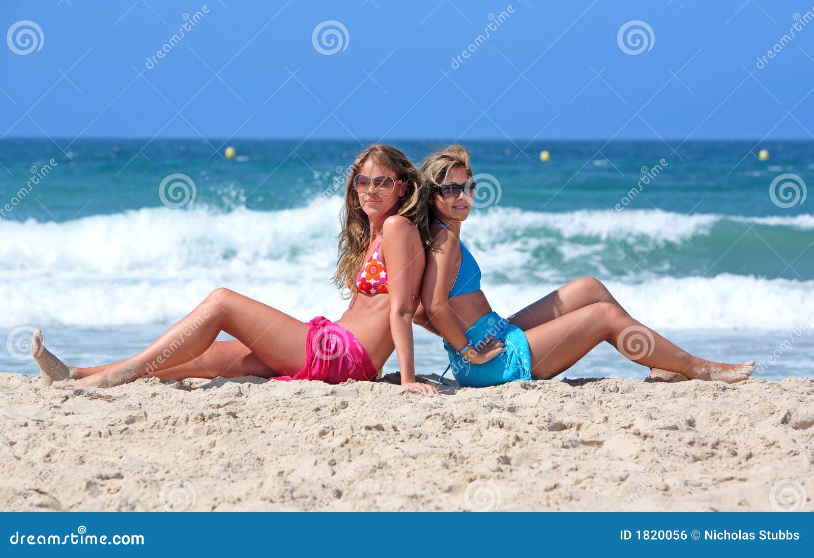 Two Young and Healthy Girls Sitting on a Sunny Beach Stock Photo photo