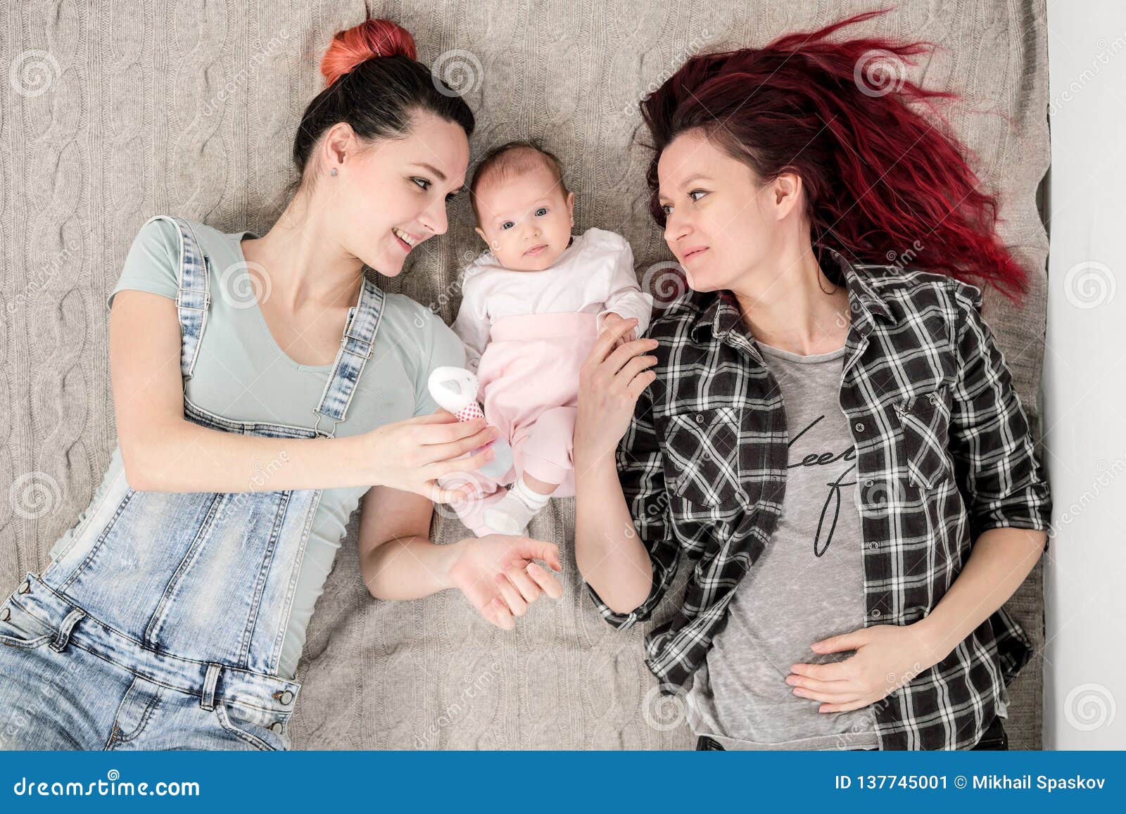 Two Young Women, a Lesbian Homosexual Couple, are Lying on a Blanket with a Child image