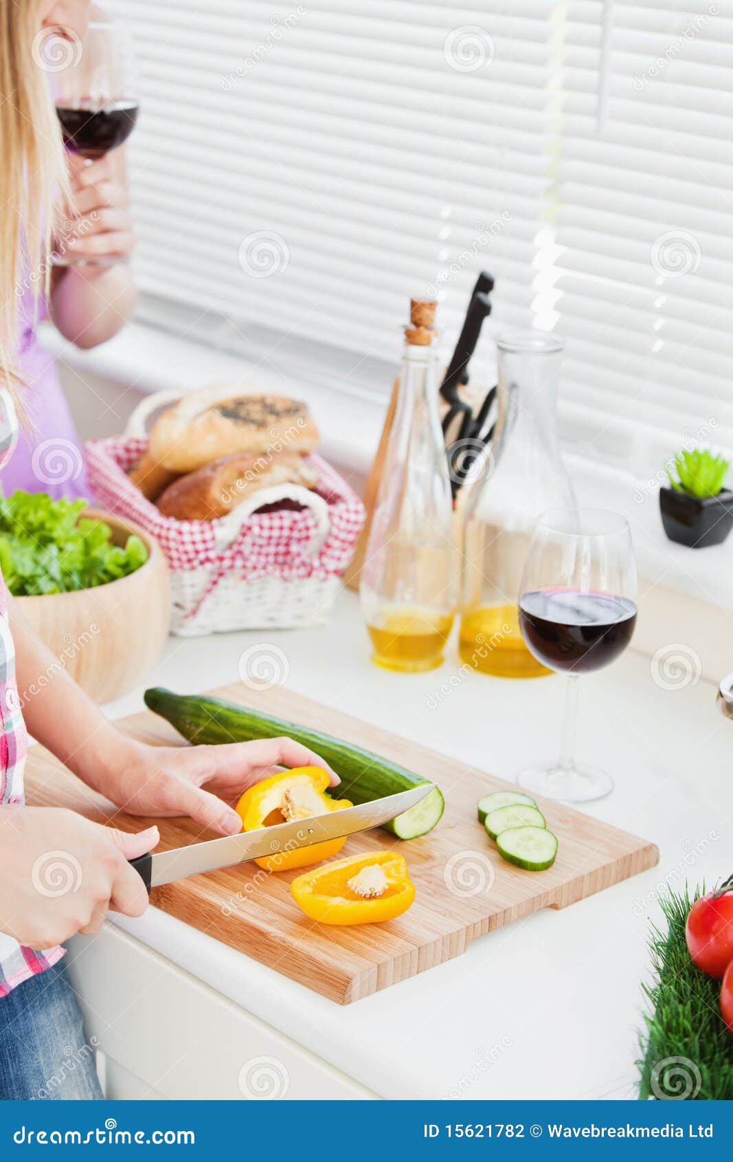 Close-up of two young women cutting paprika and cucumber for a salad in the kitchen