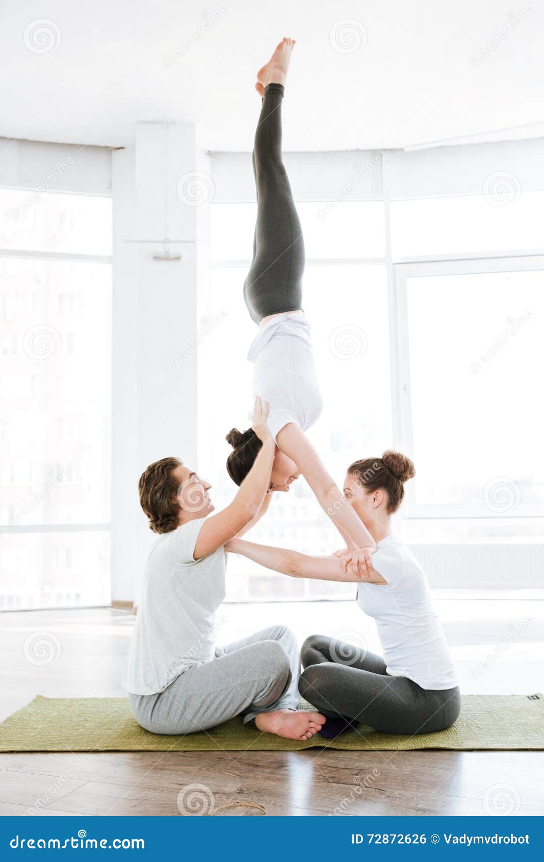 Two Young Women and Man Doing Acrobatic Yoga Position Stock Photo