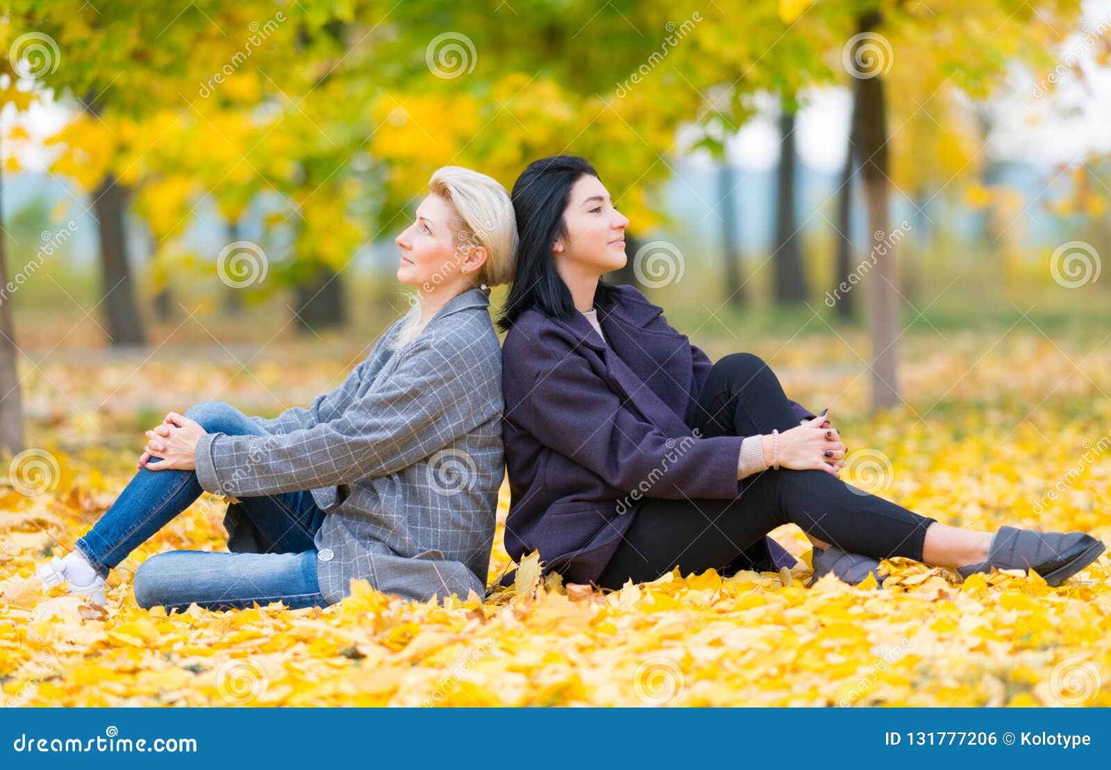 Two Young Women Sitting Back To Back in Park. Stock Photo - Image of ...