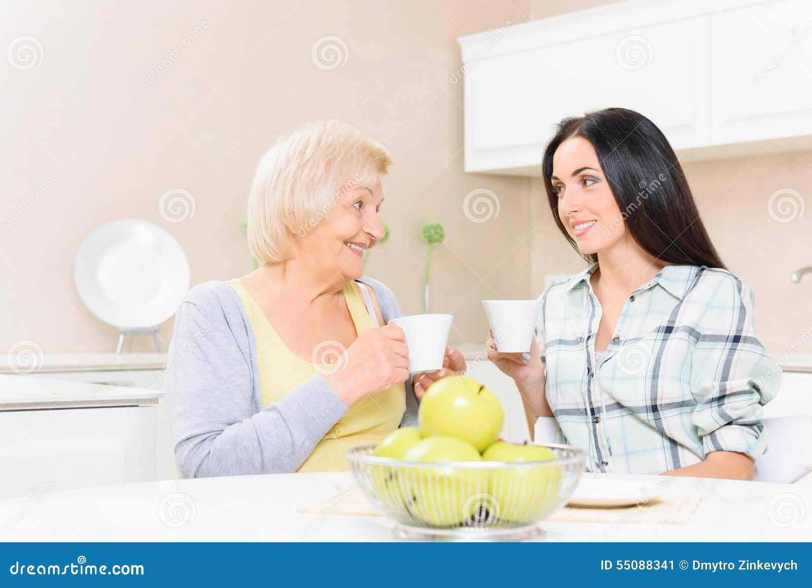Té de consumición de la abuela y de la nieta. Vistazo suave Abuela y nieta que se sientan en cocina así como las tazas de té y que miran uno a