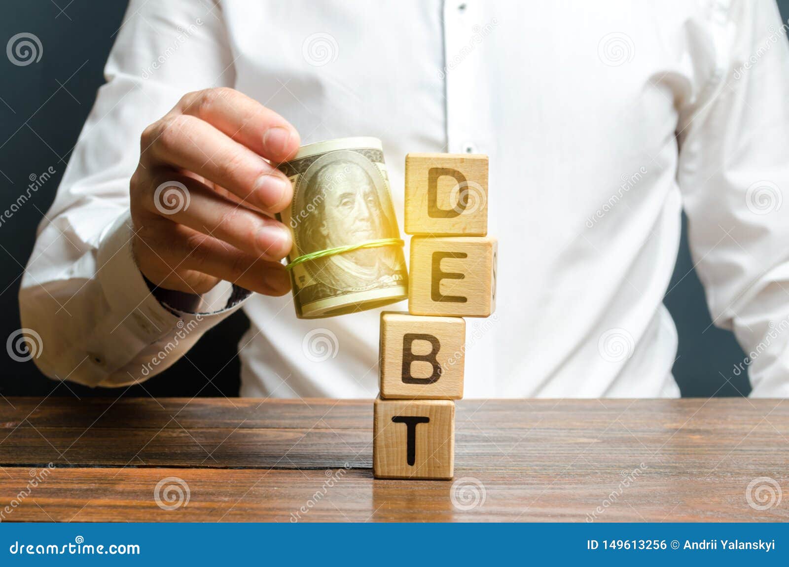 Um homem bate para baixo a torre com o d?bito da palavra com a ajuda de um pacote de dinheiro O reembolso adiantado do empr?stimo. A man knocks down the tower with the word debt with the help of a bundle of money. Early repayment of the loan, remove interest charges and pay only the loan body. Exemption from microcredit