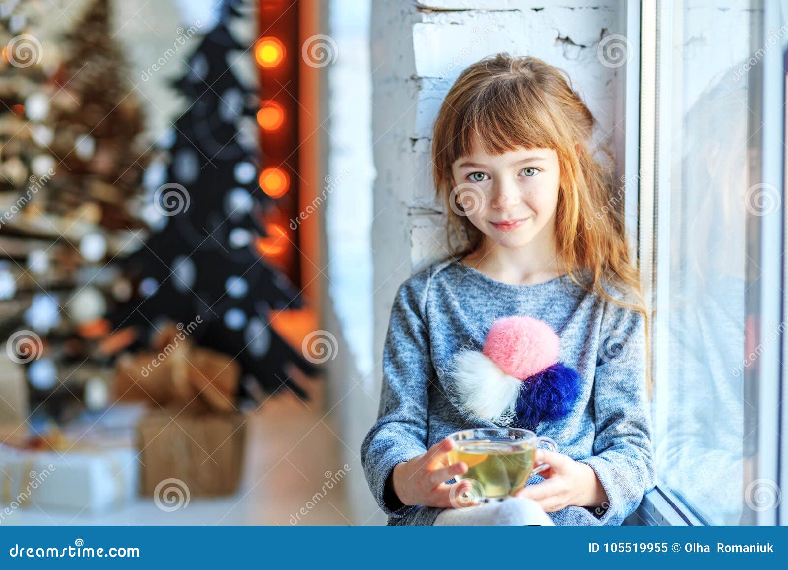 Uma criança pequena senta-se em um peitoril da janela A menina está bebendo o chá Natal feliz do conceito, ano novo, feriado, inverno, infância