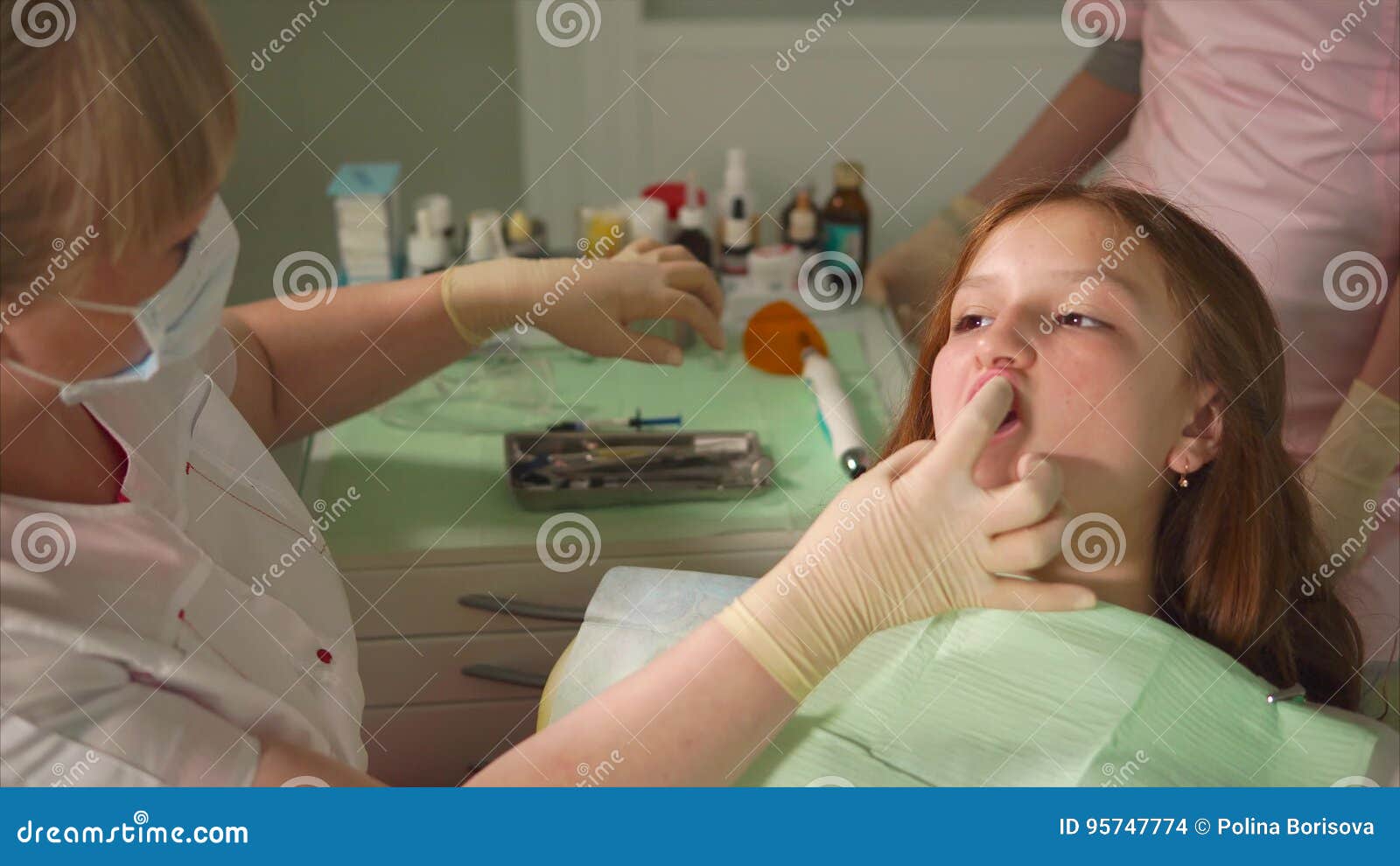 Docteur En Gants Médicaux Noirs Examine Les Dents De La Jeune Fille En  Utilisant Un Microscope Dentaire Et Un Miroir Dans Le Bureau Du Dentiste.  La Femme A Un Bavoir Du Patient