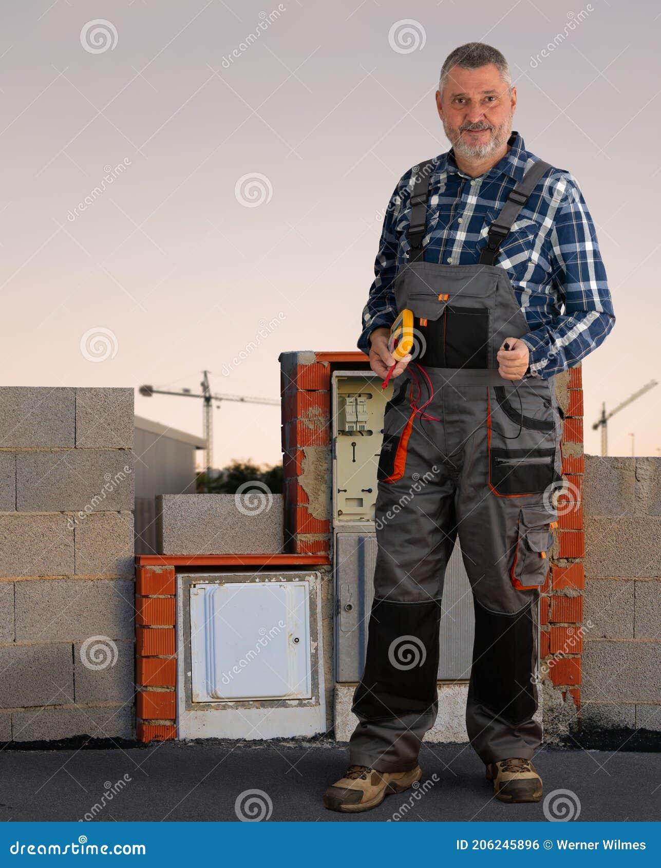 Un Electricista En Pantalones De Trabajo Está Parado En Una Construcción. Fondo Hay Grúas. Foto de archivo - Imagen de concreto, hombre: 206245896