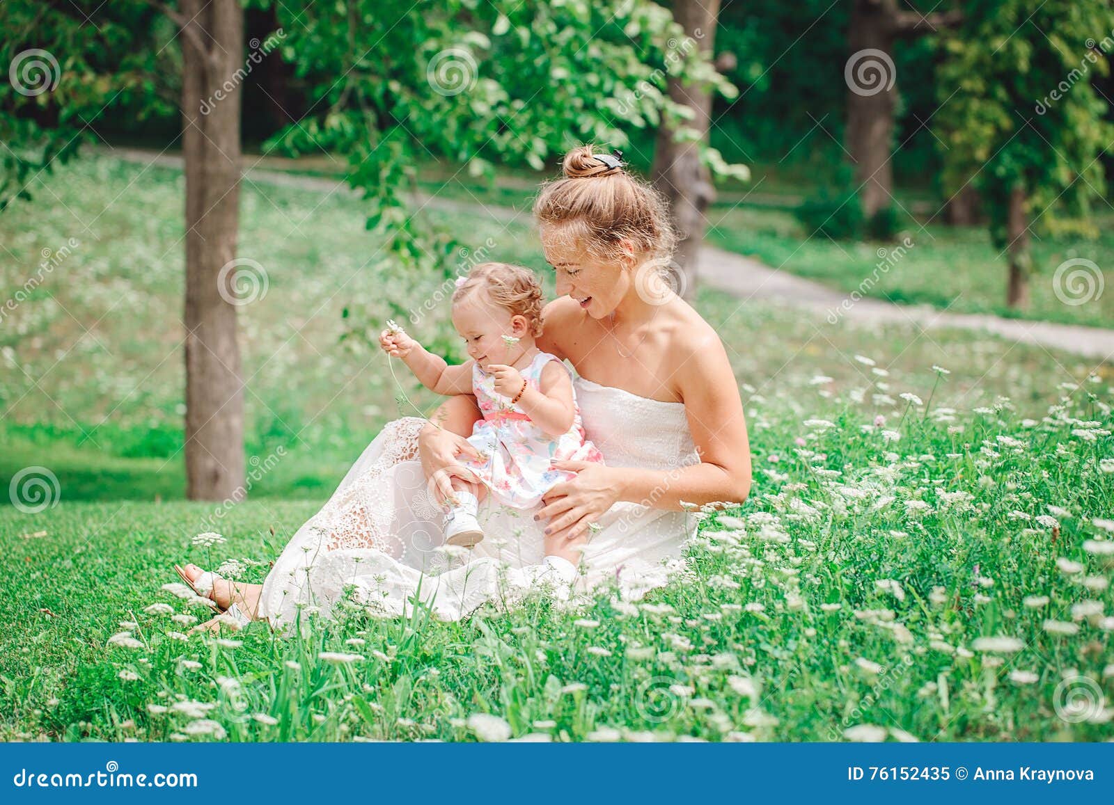 Un gruppo di due genti, di madre caucasica bianca e di bambino della neonata nel gioco di seduta del vestito bianco nella foresta verde del parco di estate fuori, guardando in camera, concetto felice di infanzia di stile di vita