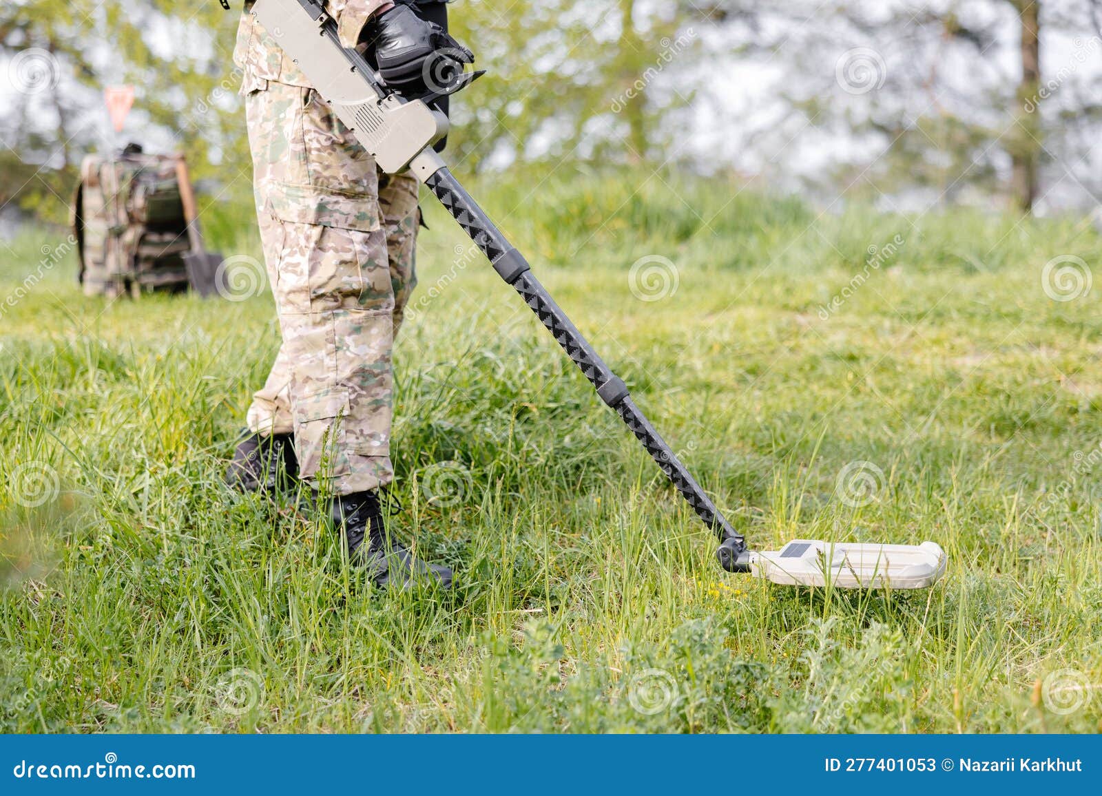 Un hombre con uniforme militar y un chaleco antibalas se sienta en el  bosque cerca de un detector de metales y una mochila militar un hombre hace  una pausa en el trabajo