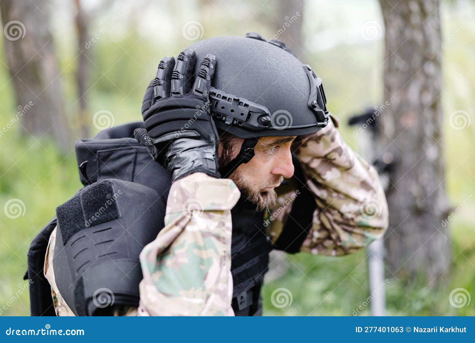 Un hombre con uniforme militar y chaleco antibalas trabaja en el bosque  para desminar el territorio