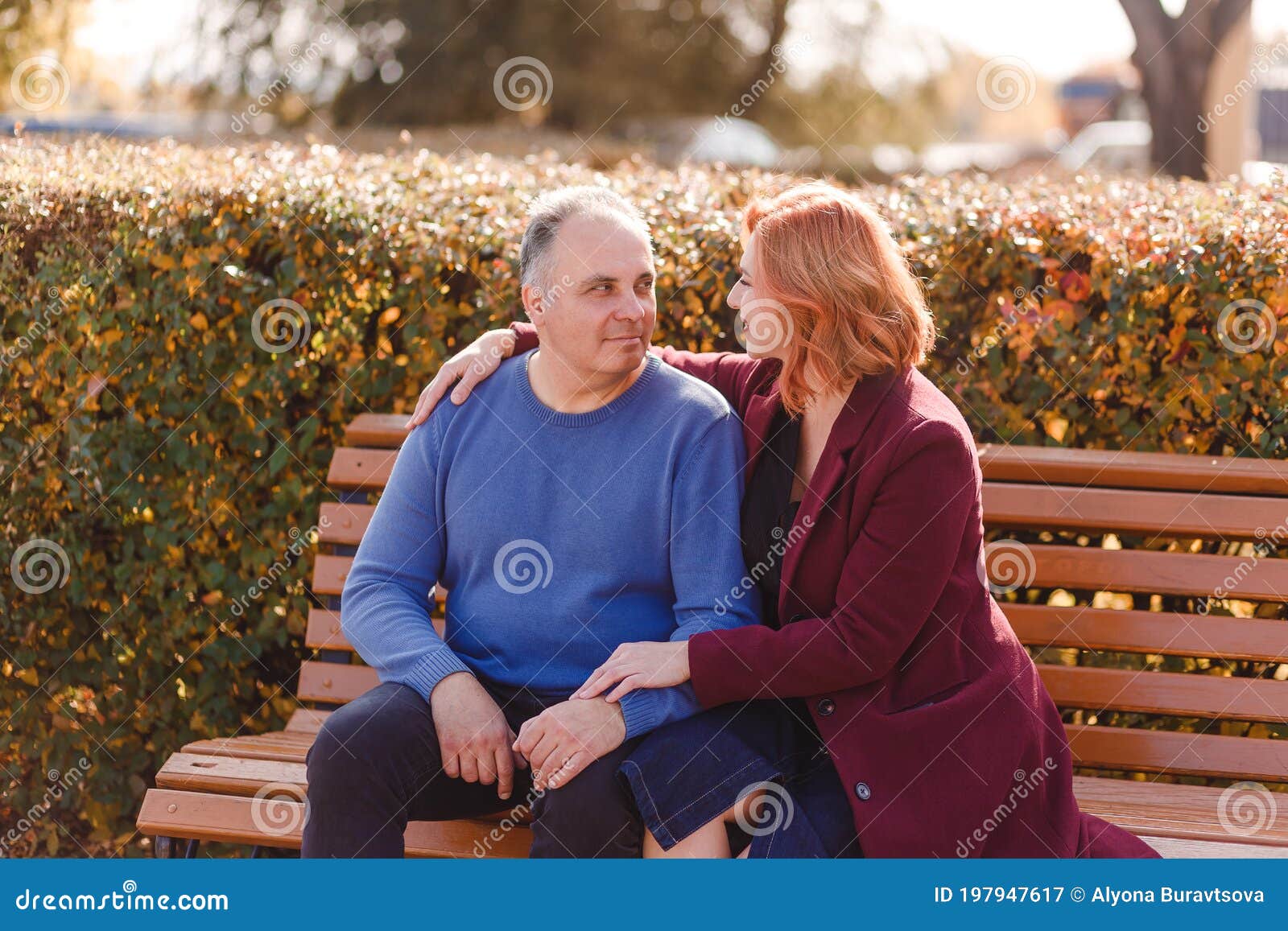 Un De 50 Años Con Un Suéter Azul Y Una Mujer Con Un Abrigo Burdeos Sentados En Un Banco De Un Parque En Otoño Imagen de archivo - Imagen de familia,