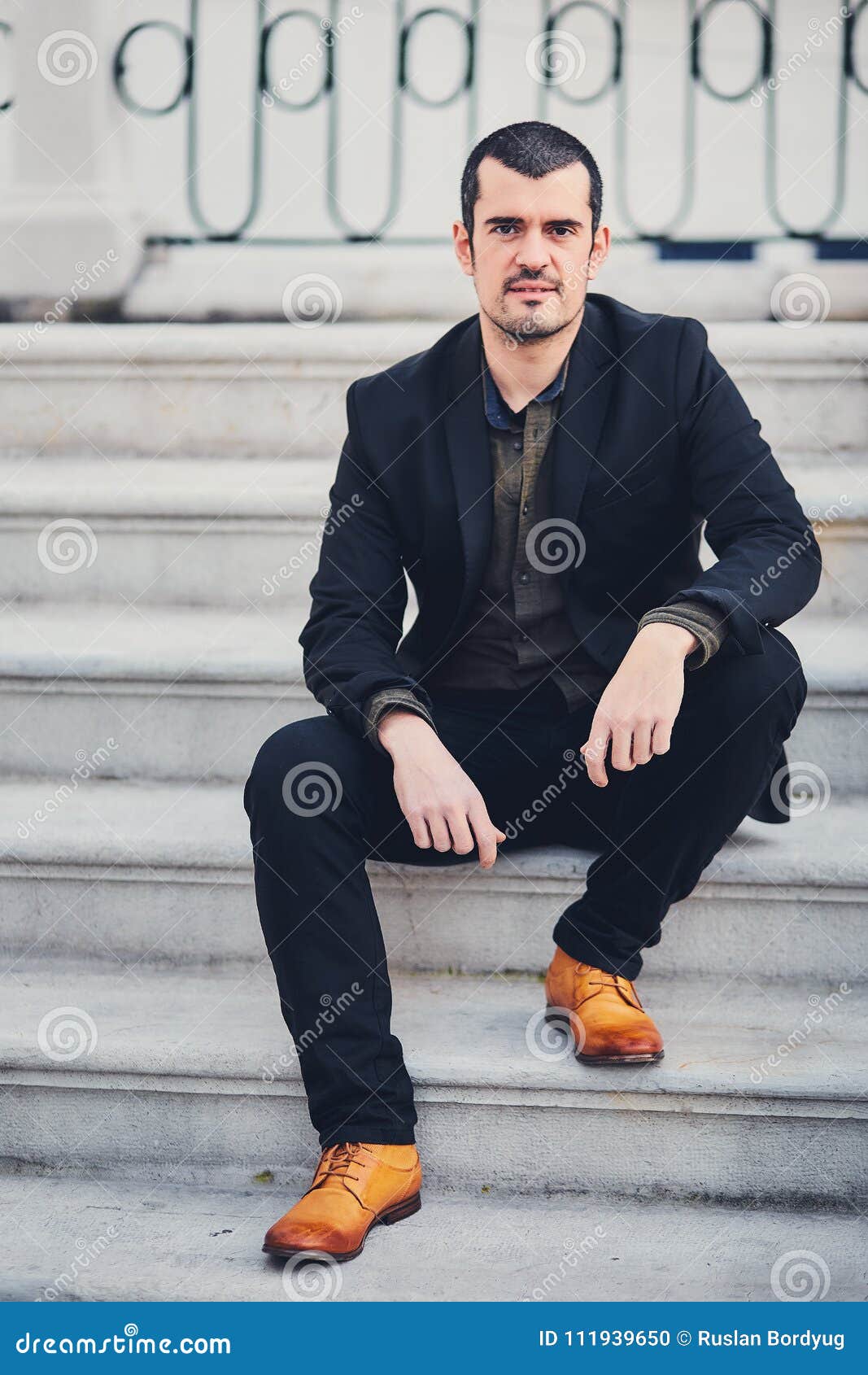 Modelo de hombre de moda en ropa elegante se sienta en la calle