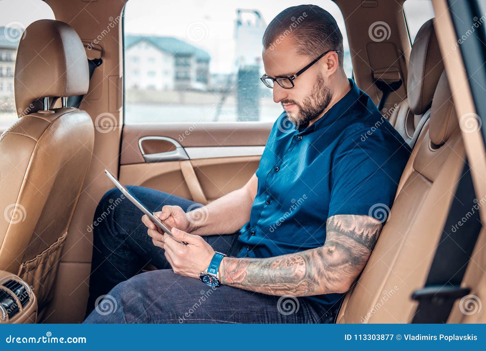 Un Homme Dans Des Lunettes Avec Le Tatouage Sur Son Bras Utilisant La  Tablette Portative Sur Un Siège Arrière D'une Voiture Image stock - Image  du intérieur, caucasien: 113303877