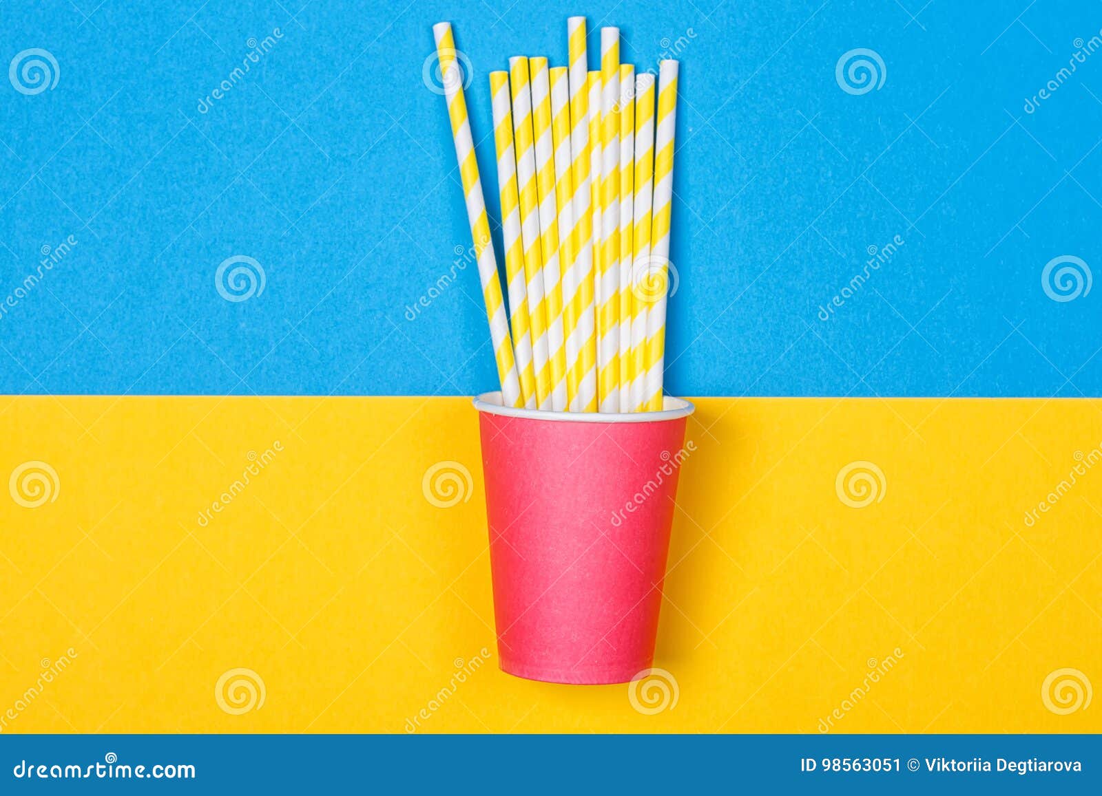 Un paquete de pajas de beber multicoloras en una taza de papel en un fondo amarillo y azul Moda mínima Endecha plana