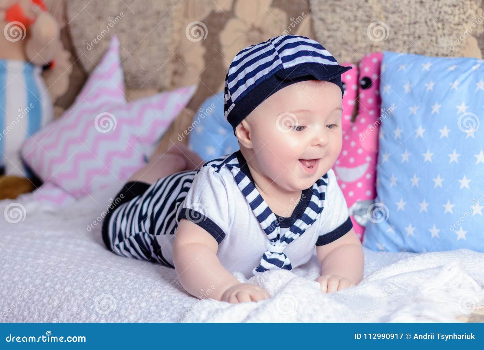 Un pequeño niño dulce en una camisa rayada y los sombreros que mienten en el sofá en las almohadas