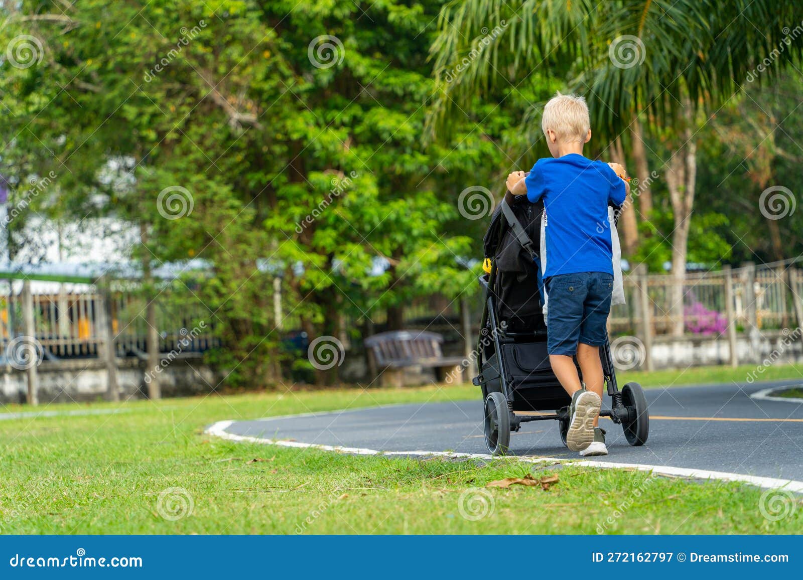 Un Petit Garçon Pousse Un Bébé Dans Une Poussette. Image stock