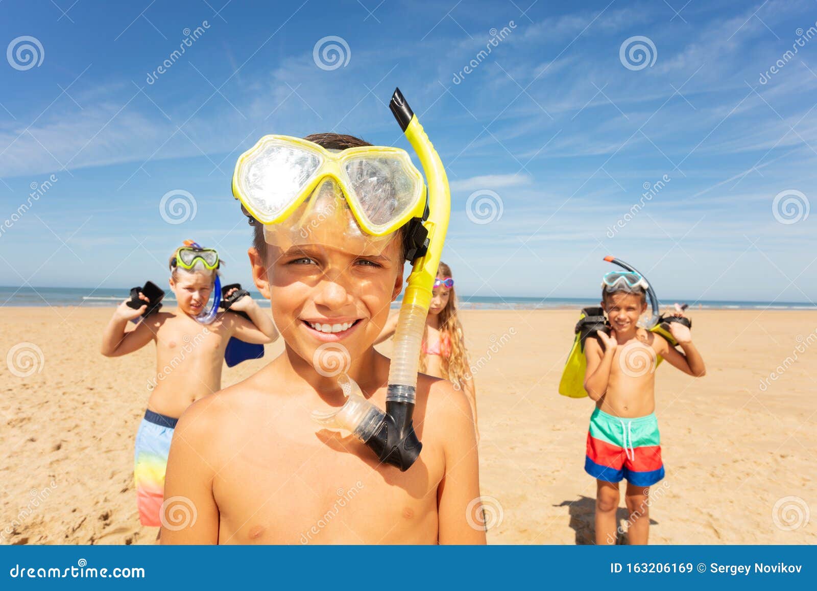Un ragazzo mascherato, un gruppo di amici sulla spiaggia. Ritratto di un ragazzo carino in un gruppo di bambini in piedi con una mascherina da snorkeling sulla spiaggia vicino al mare