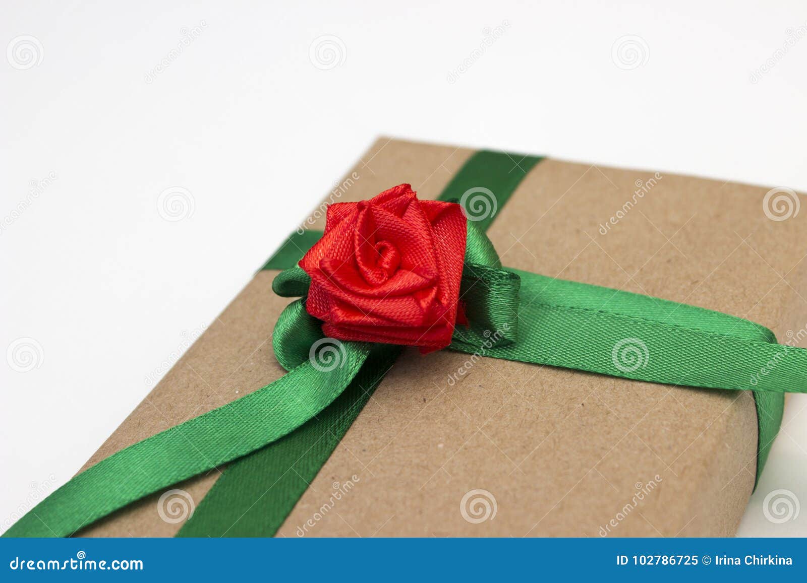 Un regalo de vacaciones envuelto en papel y atado con una cinta verde con una flor roja subió. Un regalo de vacaciones envuelto en papel y atado con una cinta verde con una flor roja de la rosa en el fondo blanco