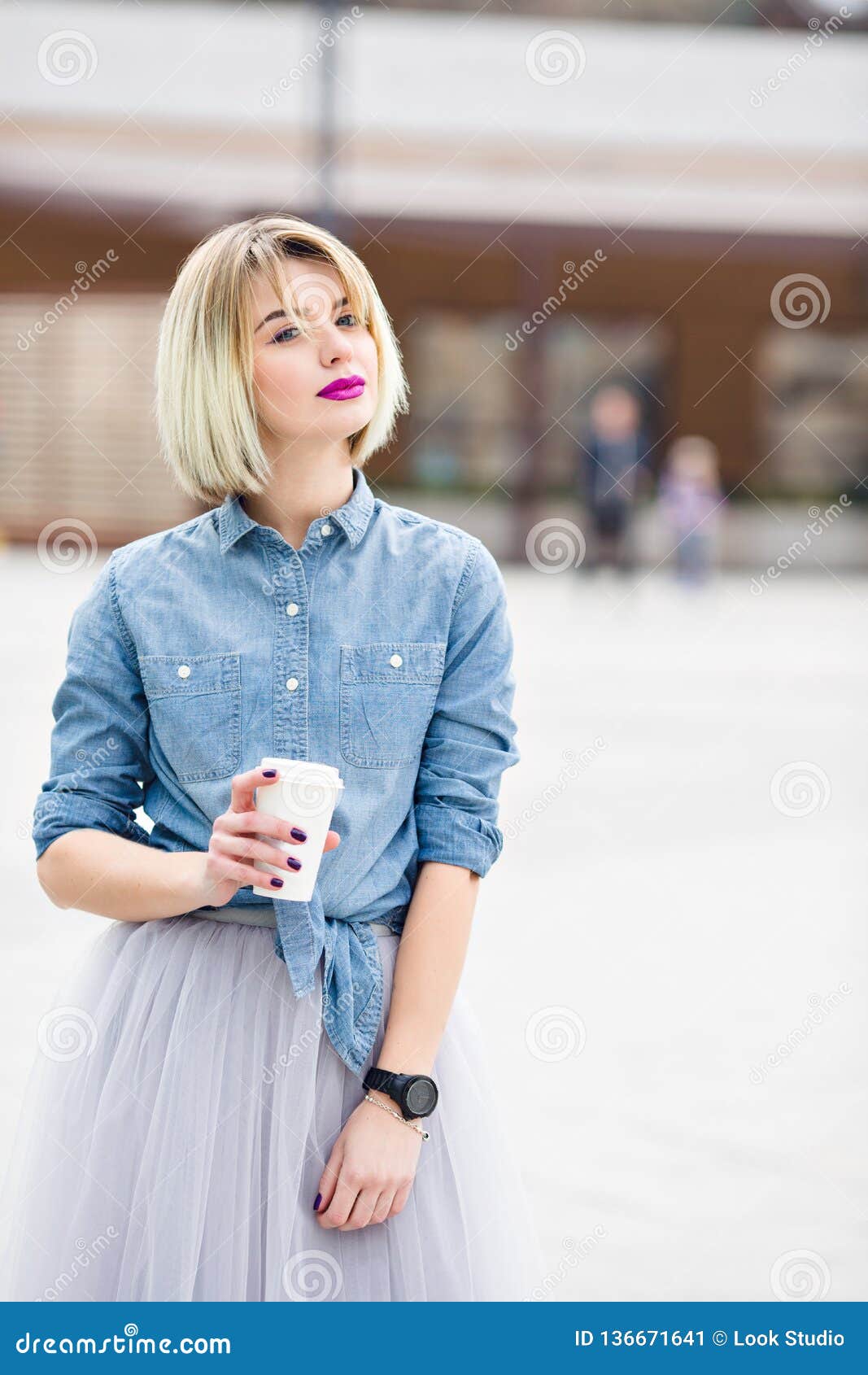 Un retrato de una muchacha rubia soñadora derecha con los labios rosados brillantes hoding una taza de camisa del dril de algodón del cofee que lleva, Tulle gris