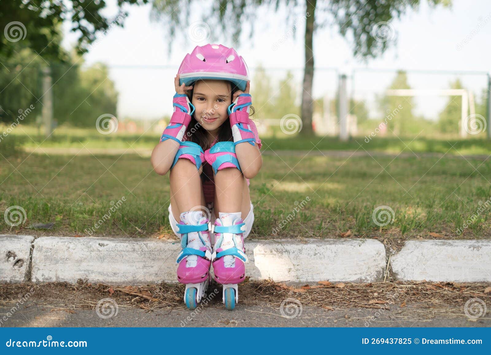 Niña hermosa en patines en un casco y protección de manos y pies en un  parque de patinaje
