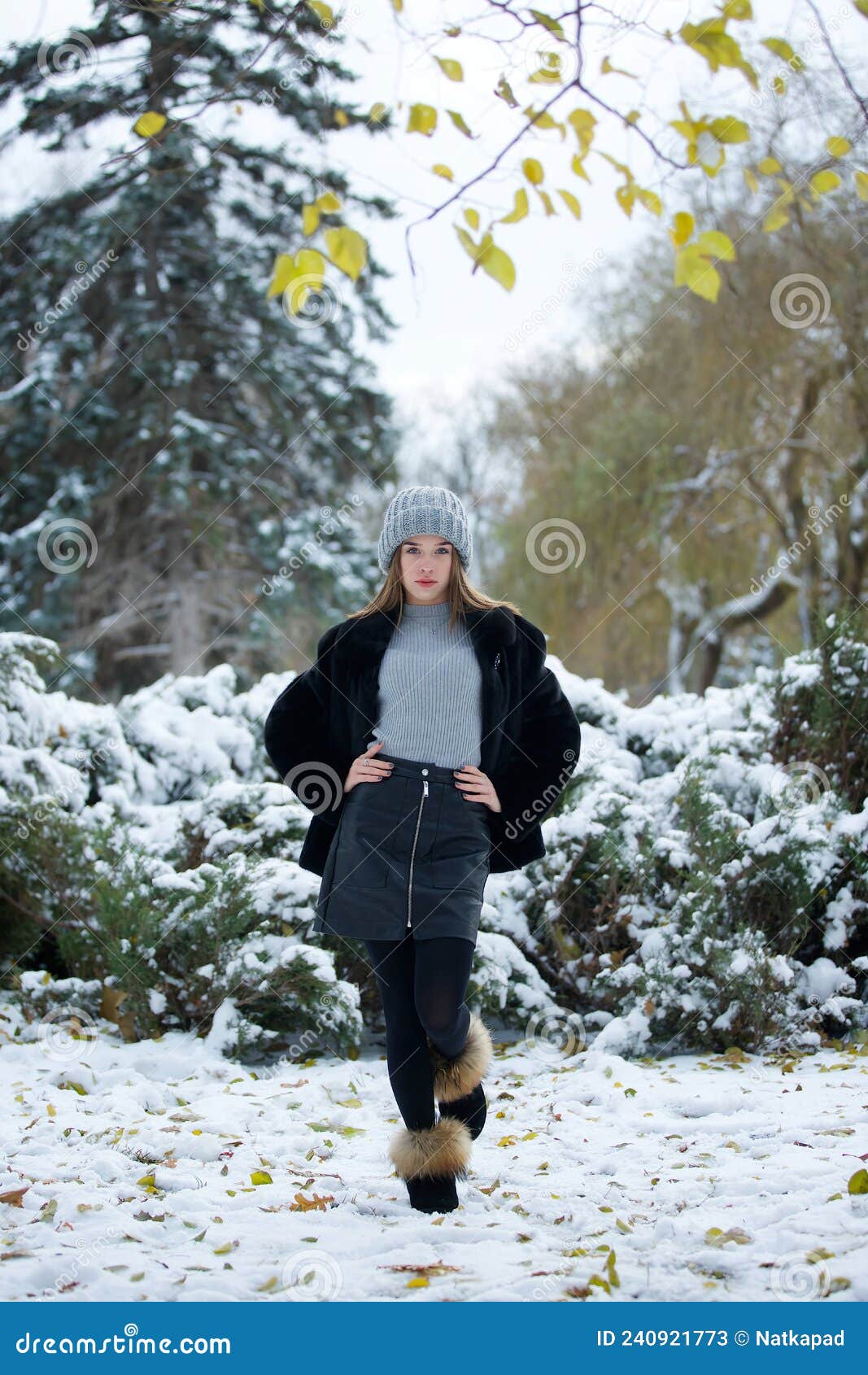 Mujer Con Ropa De Invierno Y Sombrero Caminando Al Aire Libre Bajo La Nieve.  Mujer De Pie Bajo La Luz De La Calle Mirando La Nieve Que Cae En La Noche.  País