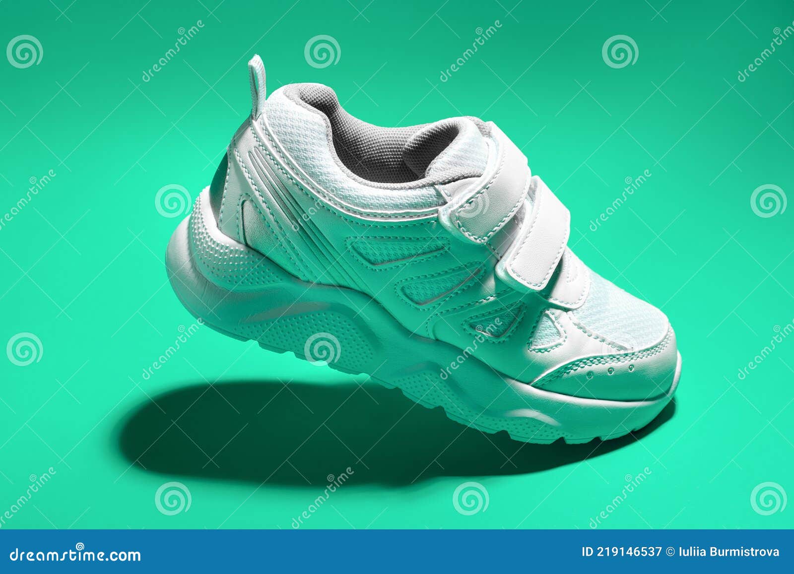 Zapatillas de deporte de niño blanco volador macro con cierres de velcro  aislado sobre un fondo azul con luz dura