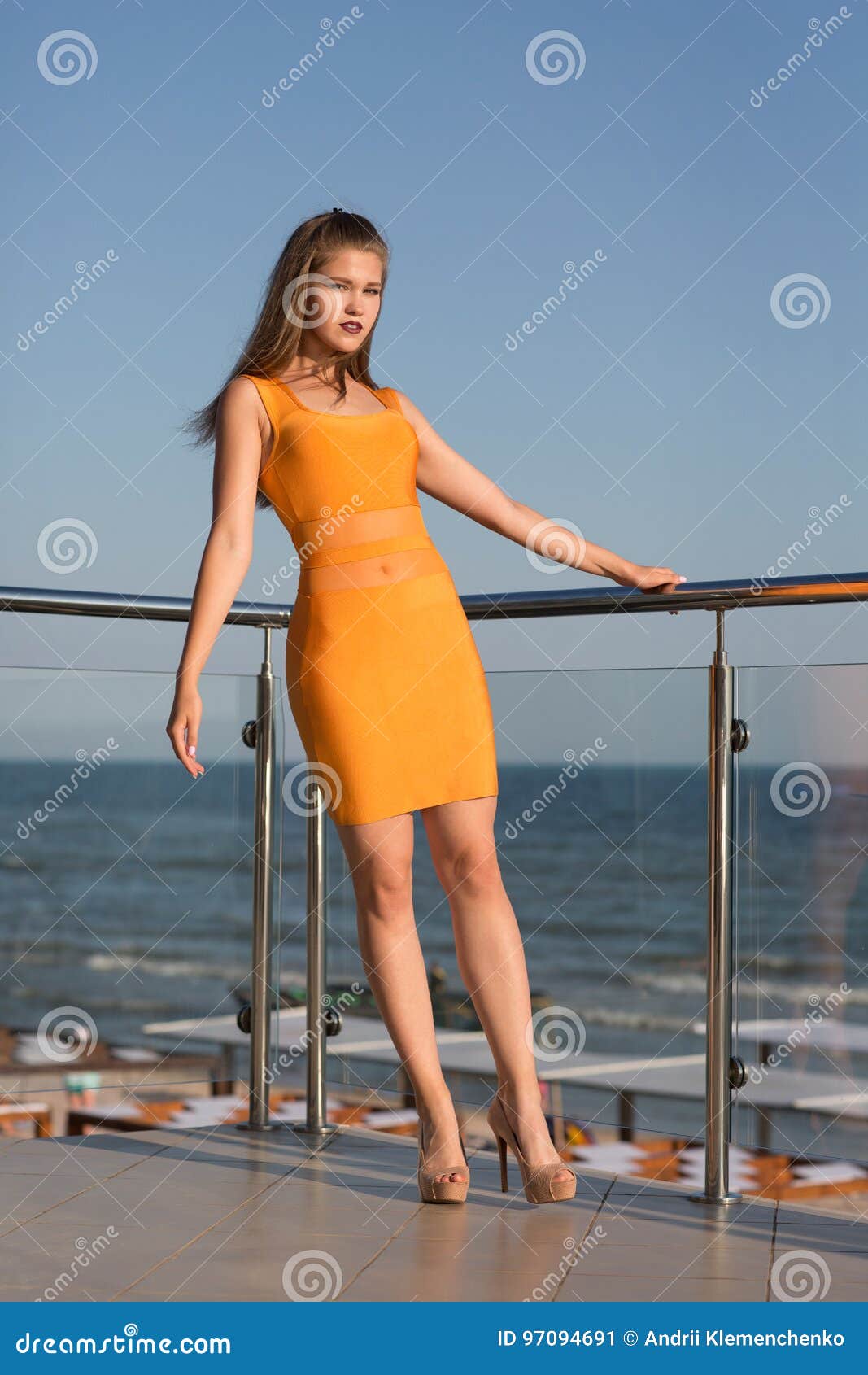 Una Muchacha Hermosa Que Presenta En Un Balcón En Un Fondo Del Cielo Azul  Una Señora Atractiva En Un Vestido Anaranjado Corto Con Imagen de archivo -  Imagen de vacaciones, hotel: 97094691