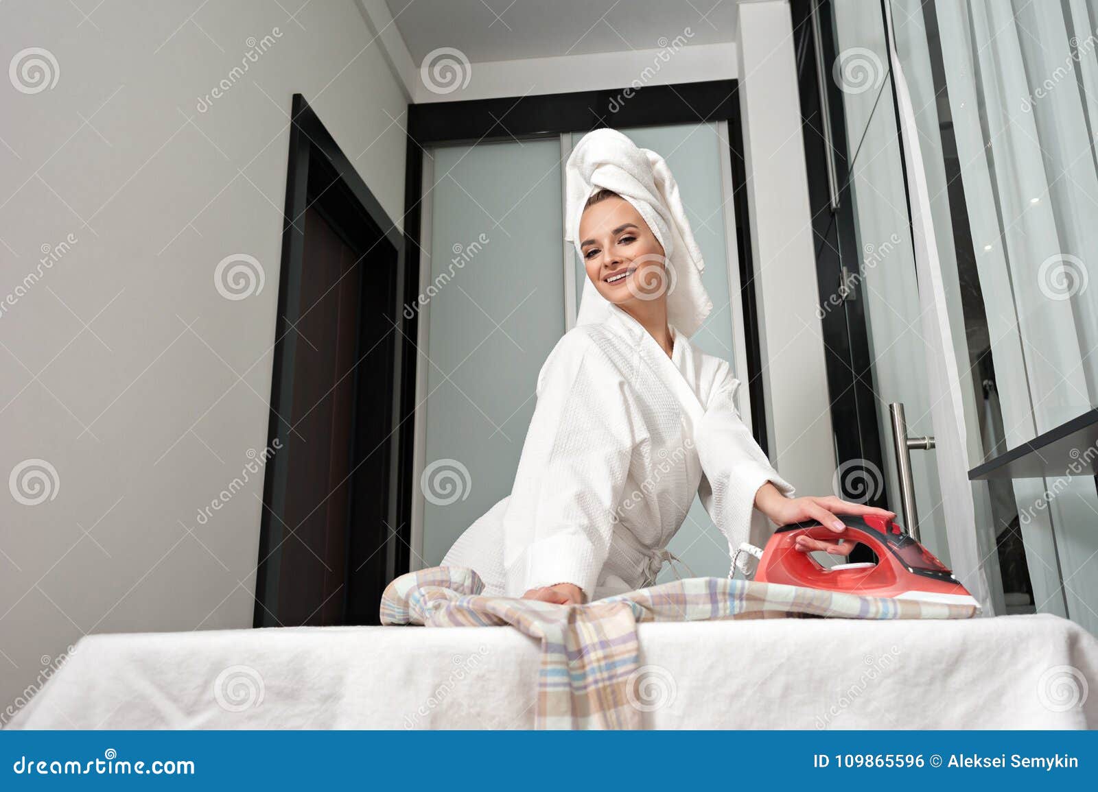 Una Mujer Alegre Joven Después De Que Una Ducha, Llevando Una Albornoz  Blanca Y Una Toalla En Su Ropa Que Plancha Principal En El Foto de archivo  - Imagen de caricia, calandre