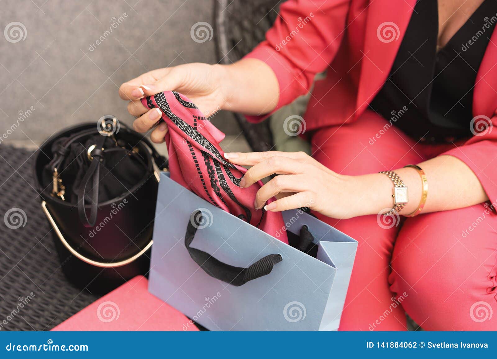 Una mujer en un pantsuit que el color del coral vivo se sienta en una silla y que saca una bufanda