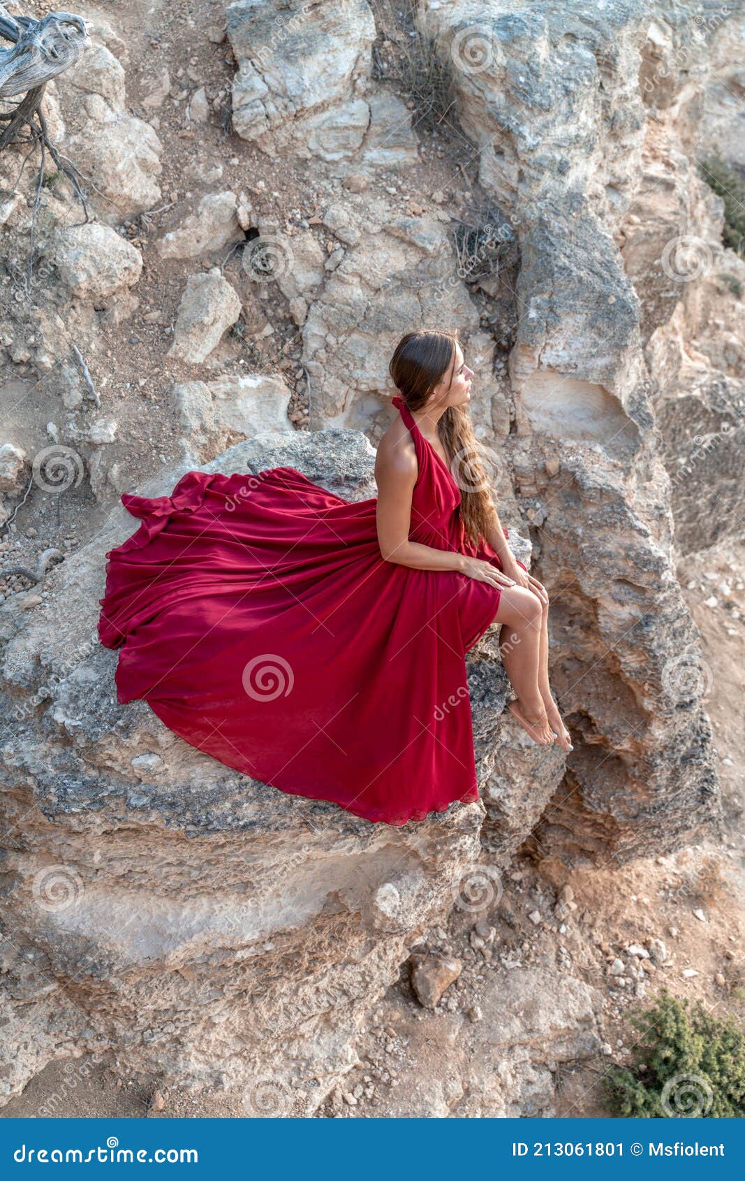 Una Niña Con El Suelto En Un Vestido Rojo Está Sentado En Una Roca De La Roca Sobre El Mar. En El Fondo Del Mar. El Concepto Imagen de archivo -