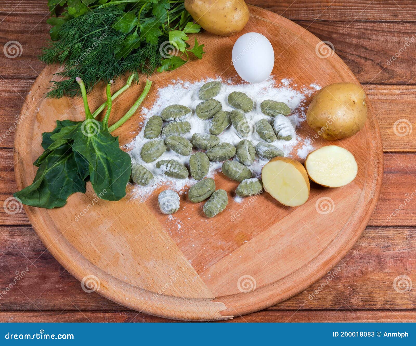 uncooked potato gnocchi with spinach, ingredients on round wooden board