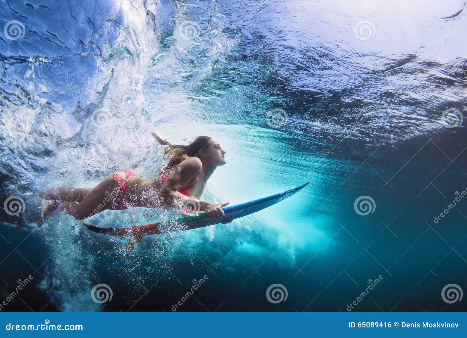 underwater photo of girl with board dive under ocean wave