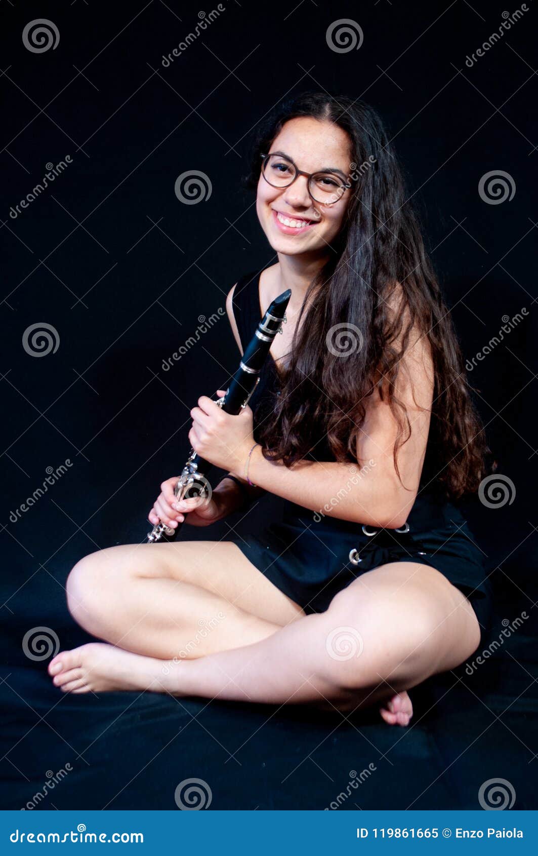 Une fille tenant son instrument de musique de clarinette Figure sur un fond noir. Une fille de brune, avec des verres, rire menteur et tenir son instrument de musique de clarinette sur un fond noir