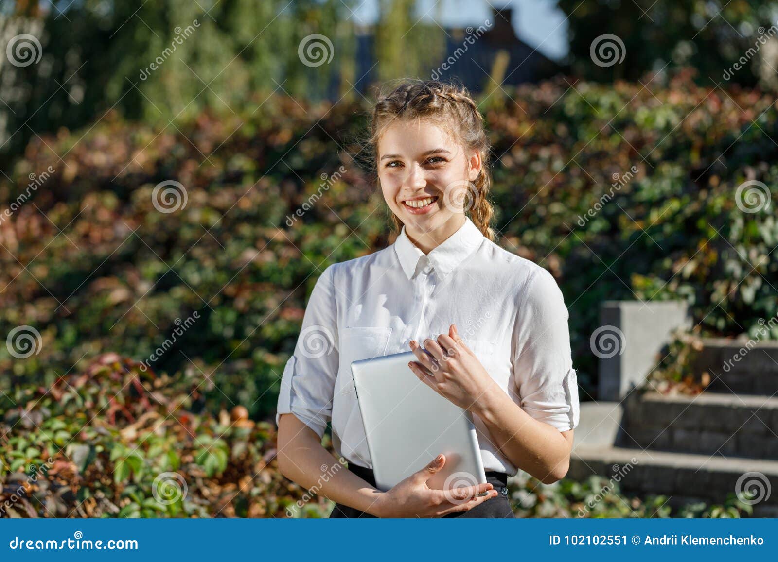 Ung flicka i parkera med en minnestavla i hand Hår flätade itu flätade trådar I en vit blus Närbild
