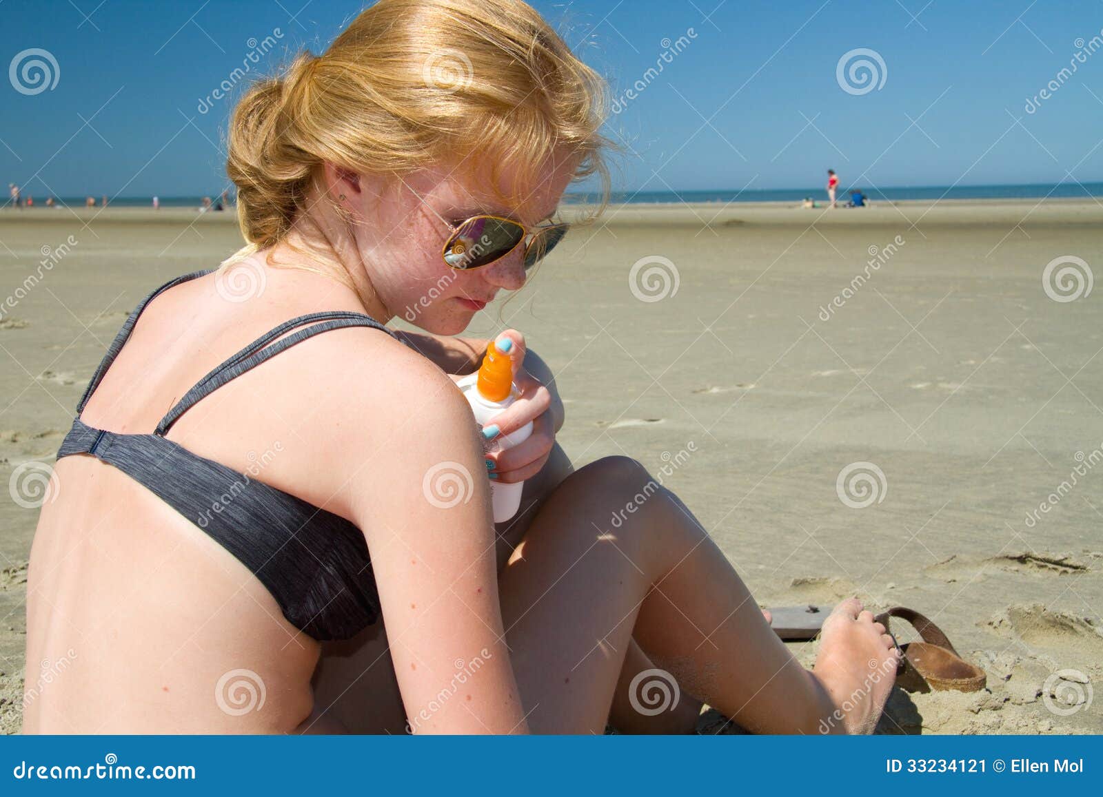 Ung flicka som besprutar solbränna på stranden på en solig dag
