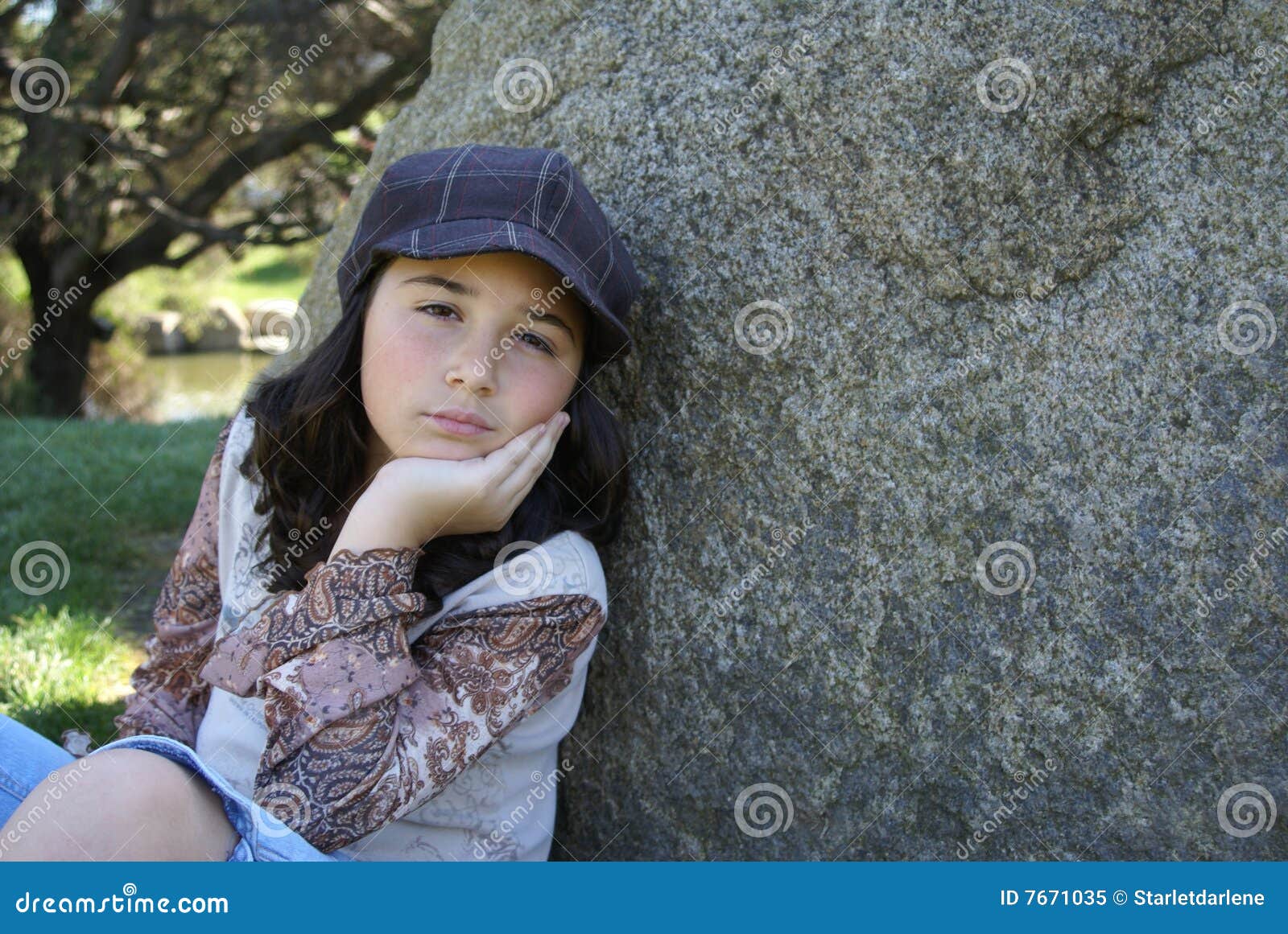 Ung flicka som sitter vid rocken i park. Ung flicka som sitter i en park vid en rock med en hatt på.