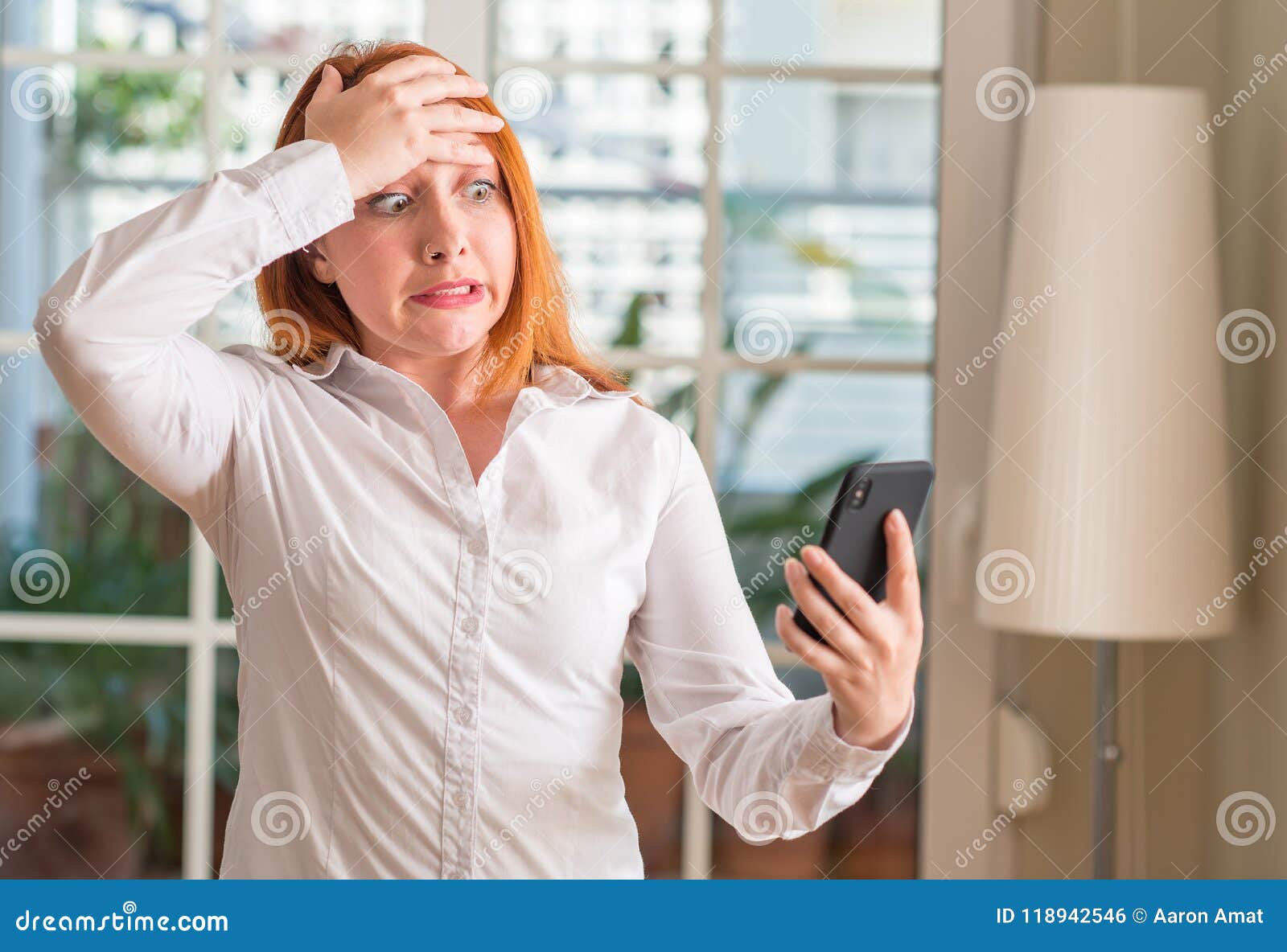 Ung härlig rödhårig mankvinna hemma. Rödhårig mankvinna som hemma som använder smartphonen är stressad med handen på huvudet som är chockat med skam- och överraskningframsidan, ilsket och frustrerat Skräck och rubbning för fel