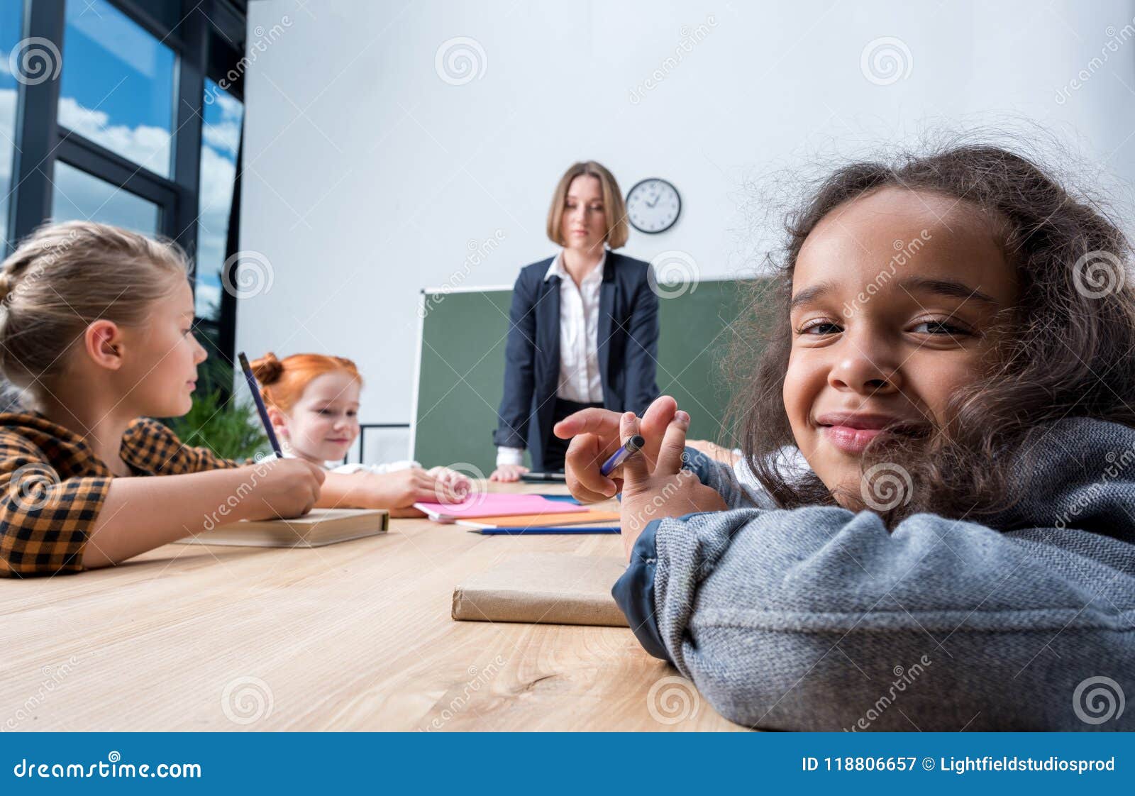 Ung lärarinna som ser multietniska skolbarn som skriver med blyertspennor på kursen