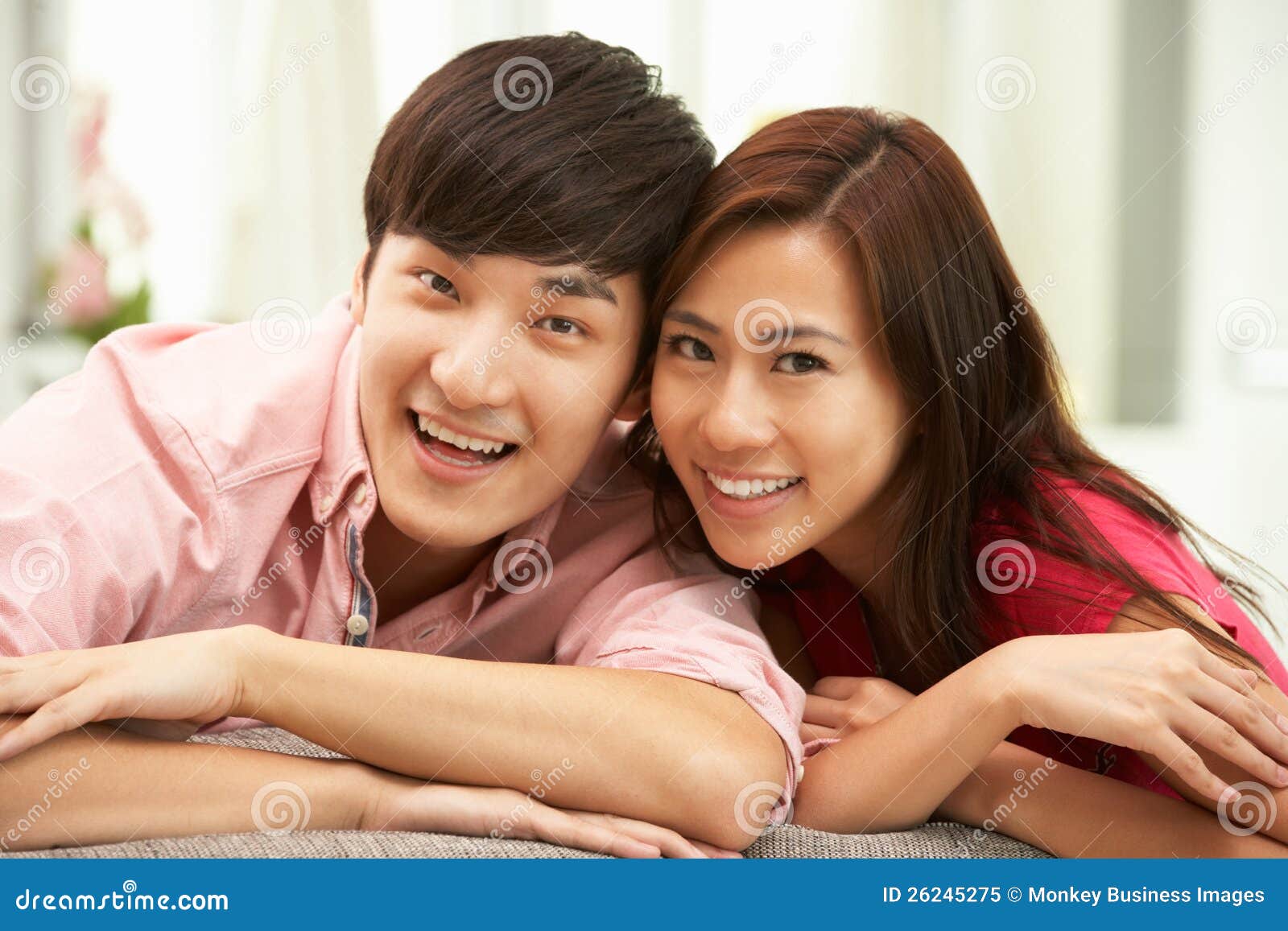 Unga kinesiska par som hemma kopplar av på sofaen. Unga kinesiska par som kopplar av på hemmastatt le för Sofa på kameran