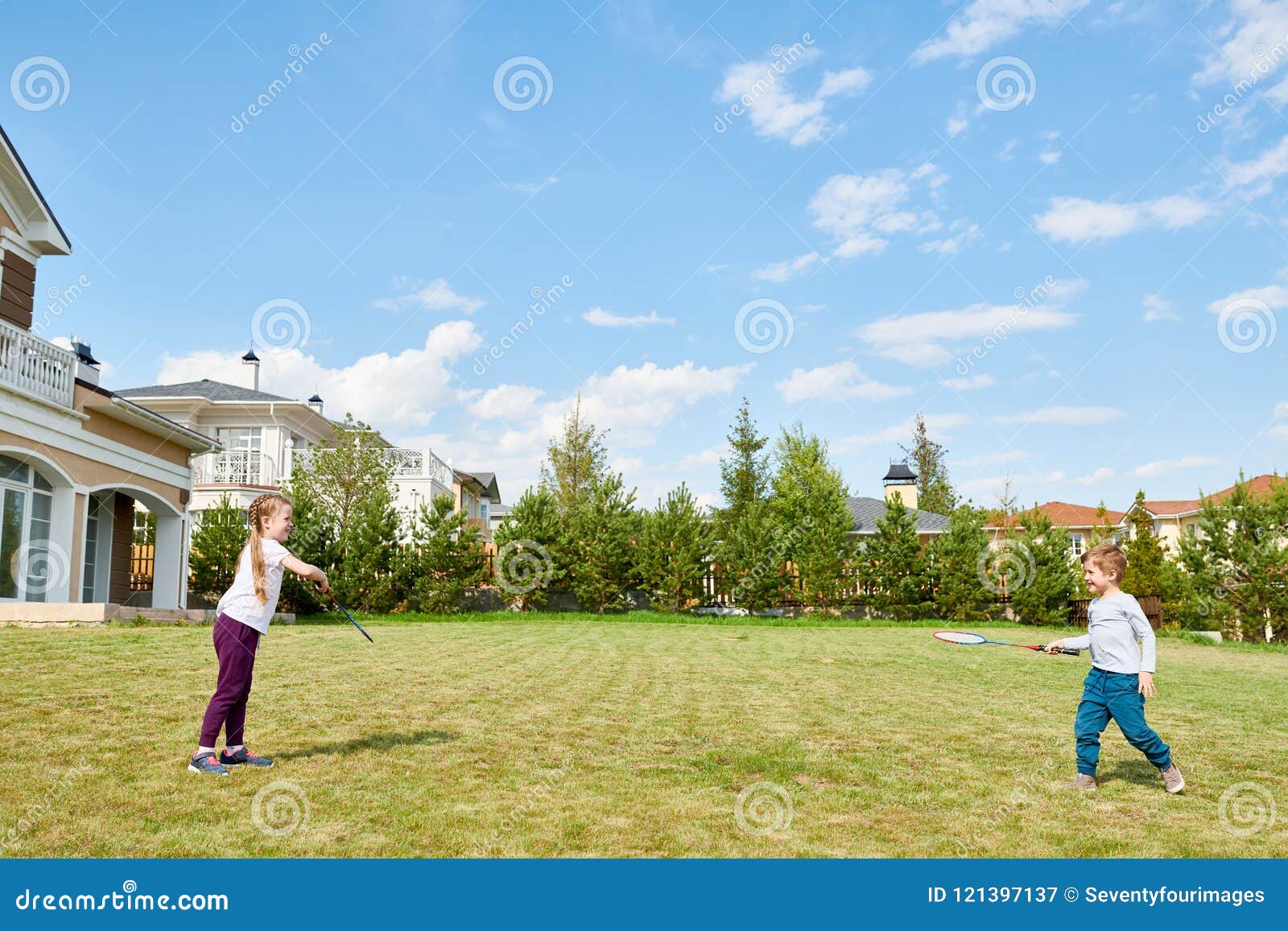 Ungar som spelar badminton i Front Yard. Full längdstående av två barn som spelar badminton på den främsta gården för grön gräsmatta som utomhus tycker om solig sommardag, kopieringsutrymme