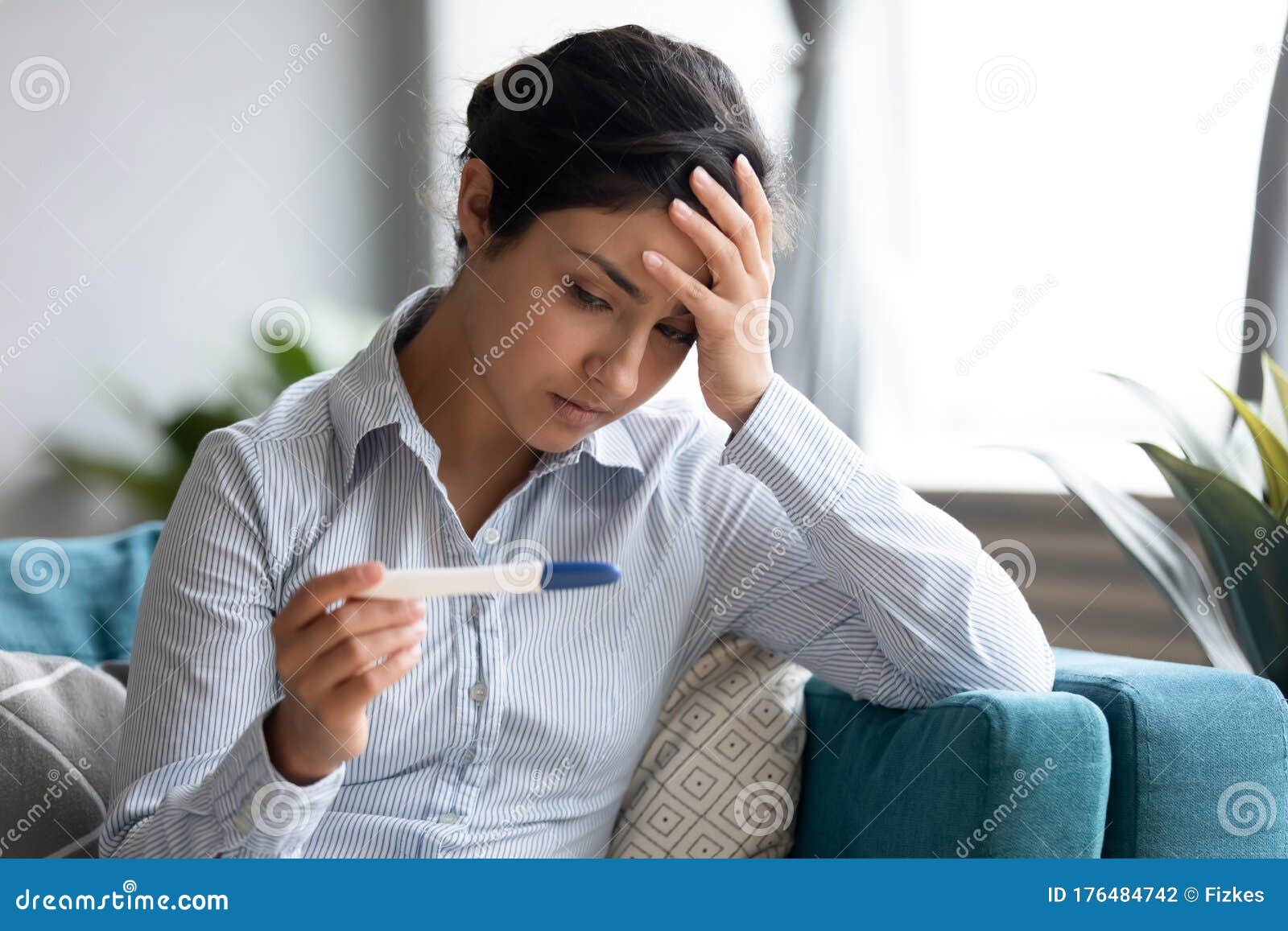 unhappy indian woman looking at pregnancy test, upset by result