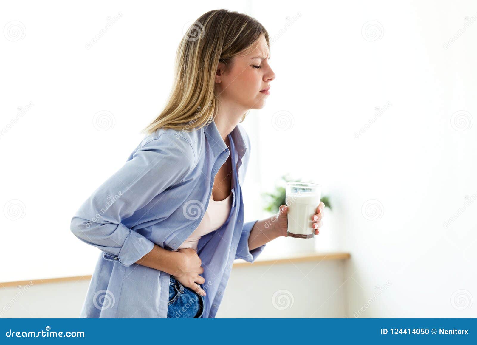 unhealthy young woman with stomachache holding a glass with milk at home.